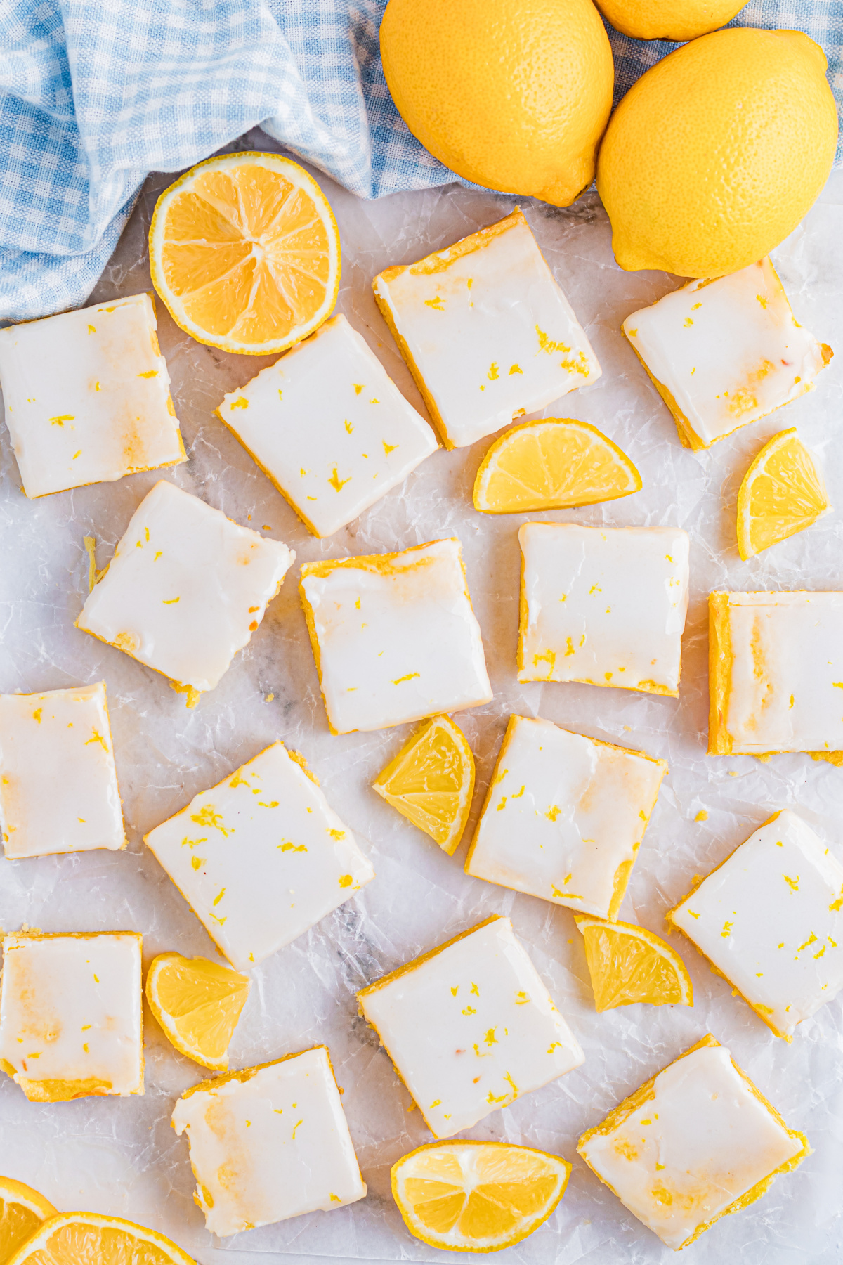 Lemon blondies arranged across parchment with fresh lemon slices, showing the glazed tops and clean, square cuts.