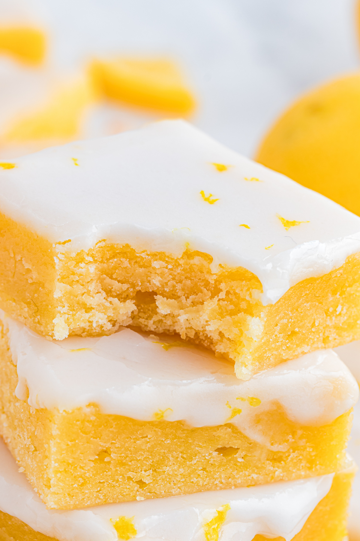 Close-up of lemon blondies stacked to show a soft, dense crumb and smooth lemon glaze with fresh zest on top.