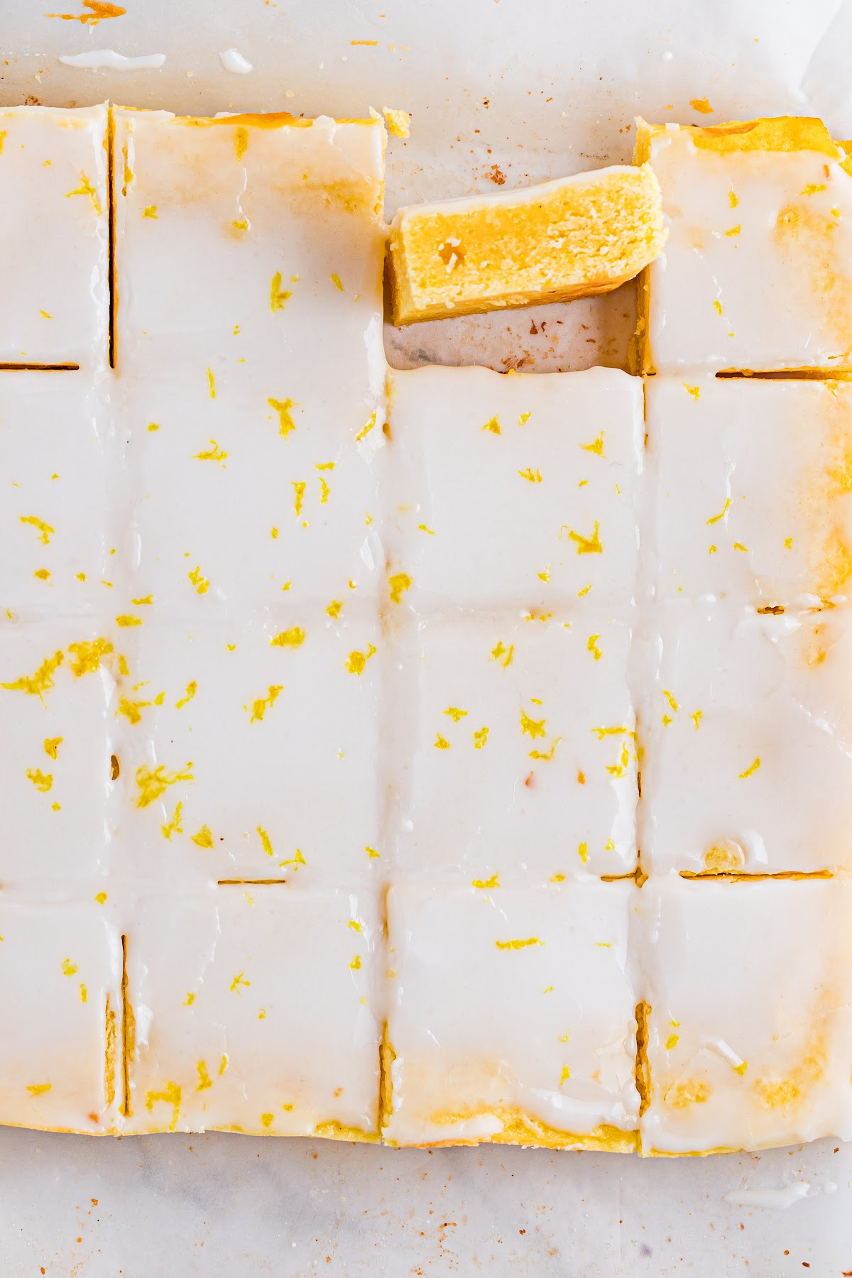 Overhead view of sliced lemon blondies in the pan, showing a smooth lemon glaze, clean cuts, and a dense yellow crumb.