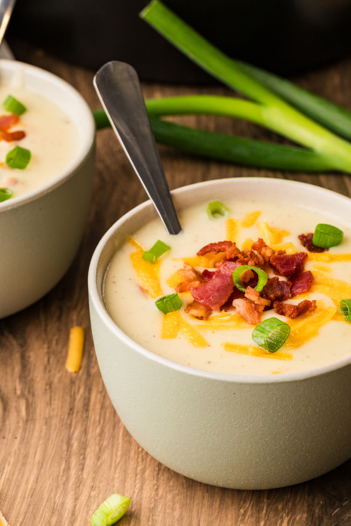 A bowl of thick, creamy potato soup topped with crisp bacon, shredded cheddar, and sliced scallions.