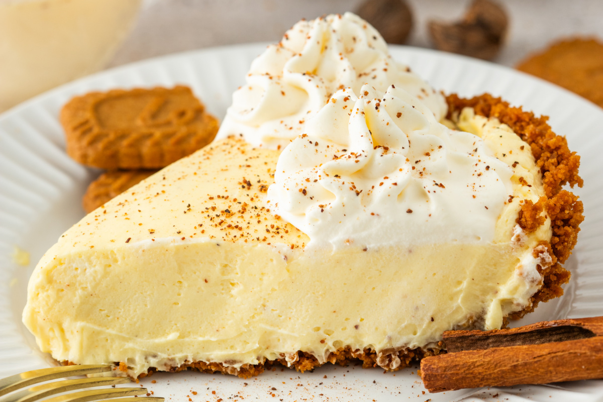 A sliced piece of eggnog cream pie showing a thick, creamy filling, a sturdy cookie crust, and a swirl of whipped cream dusted with nutmeg.