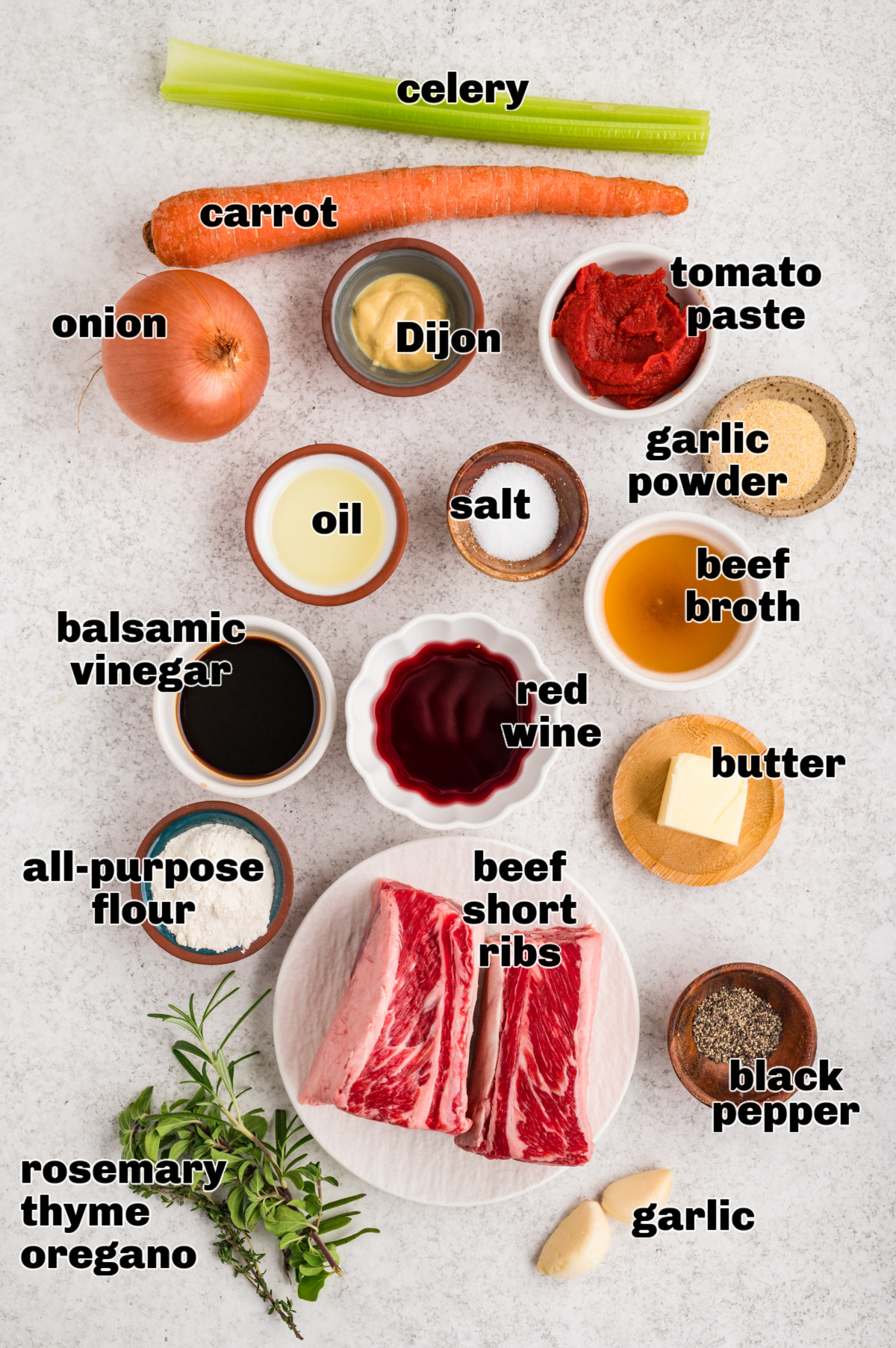 Ingredients laid out for oven-braised beef short ribs, including bone-in short ribs, vegetables, herbs, broth, wine, and seasonings.
