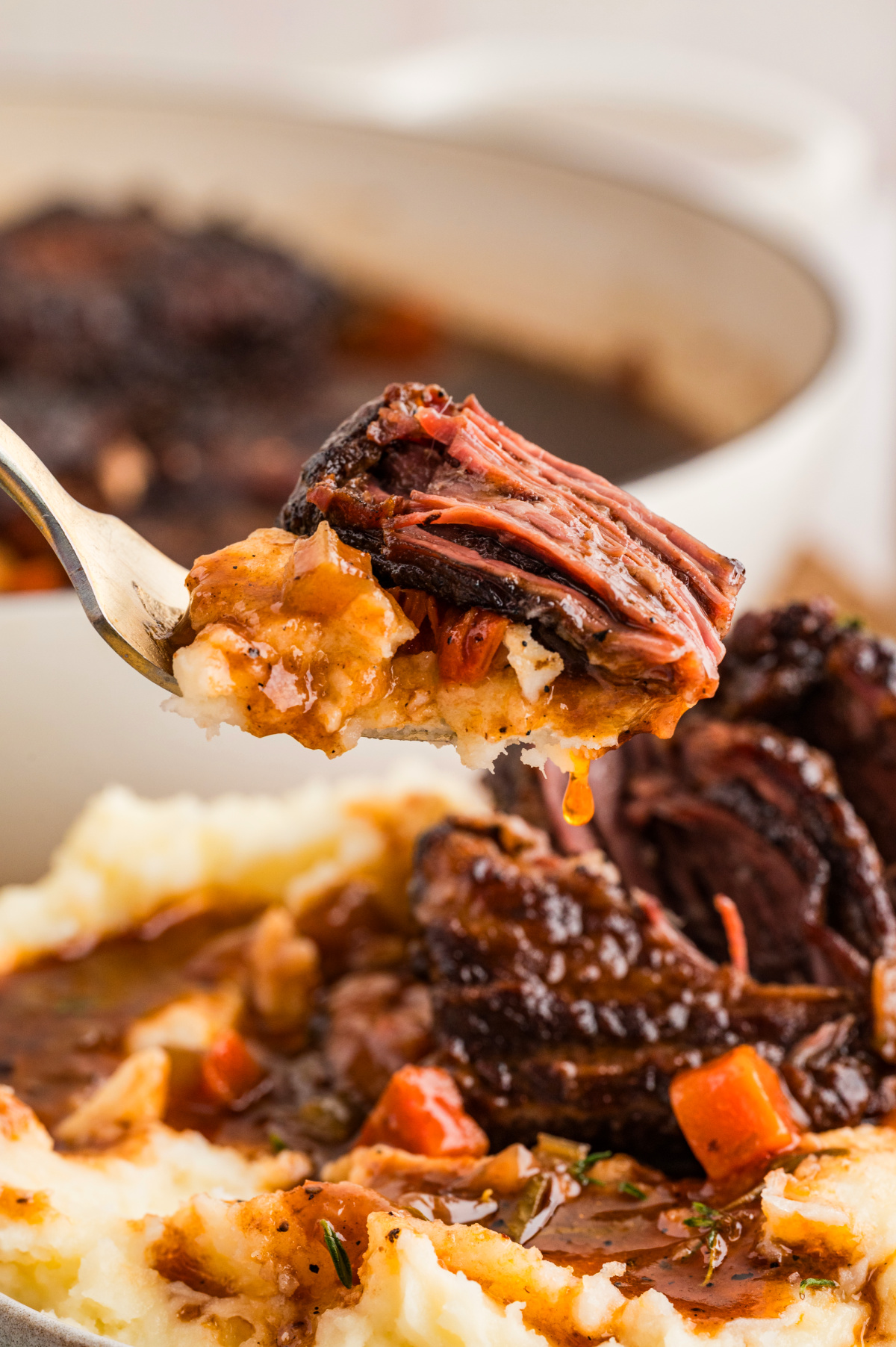 A fork lifting a bite of oven-braised short ribs with mashed potatoes and sauce, showing the meat pulling apart easily after slow cooking.