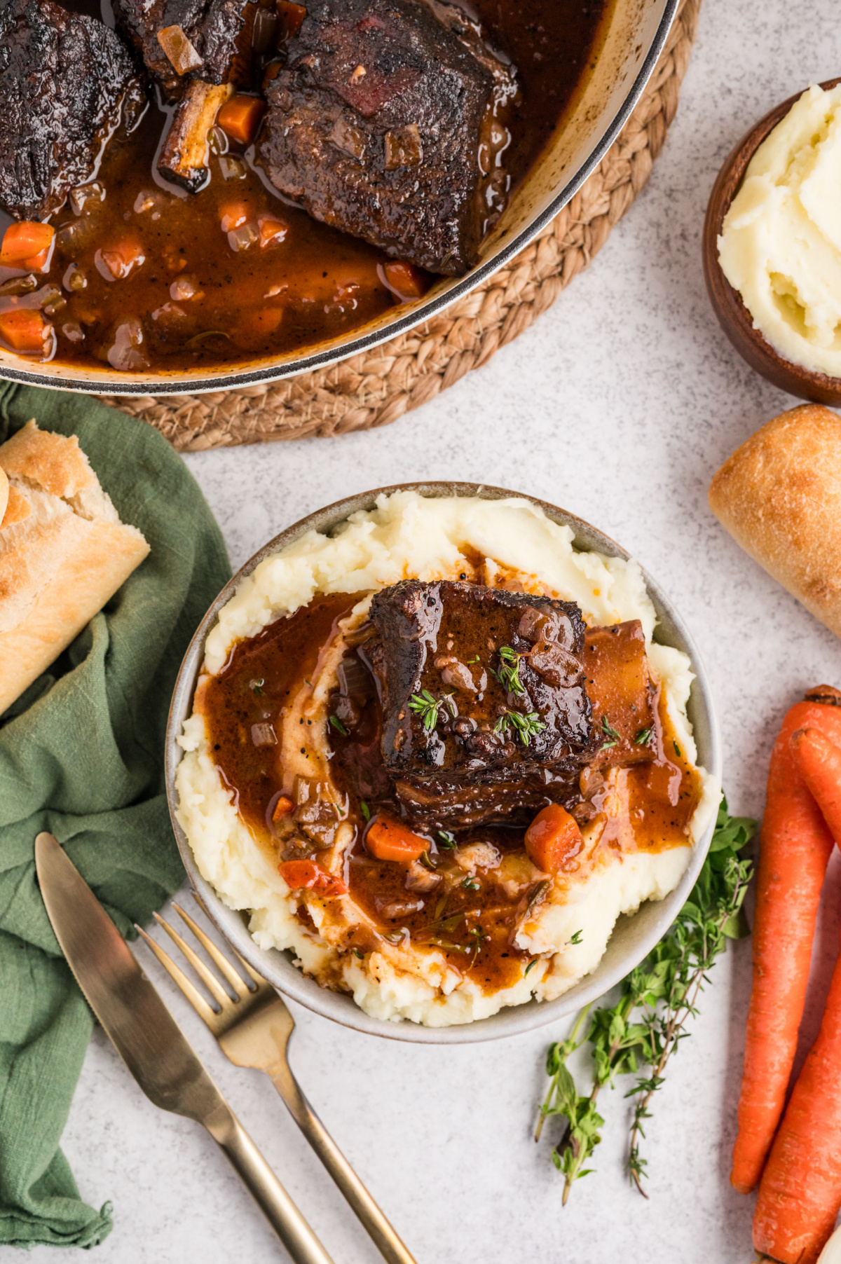 Braised beef short ribs served over mashed potatoes, finished with thick sauce, carrots, and fresh thyme on top.