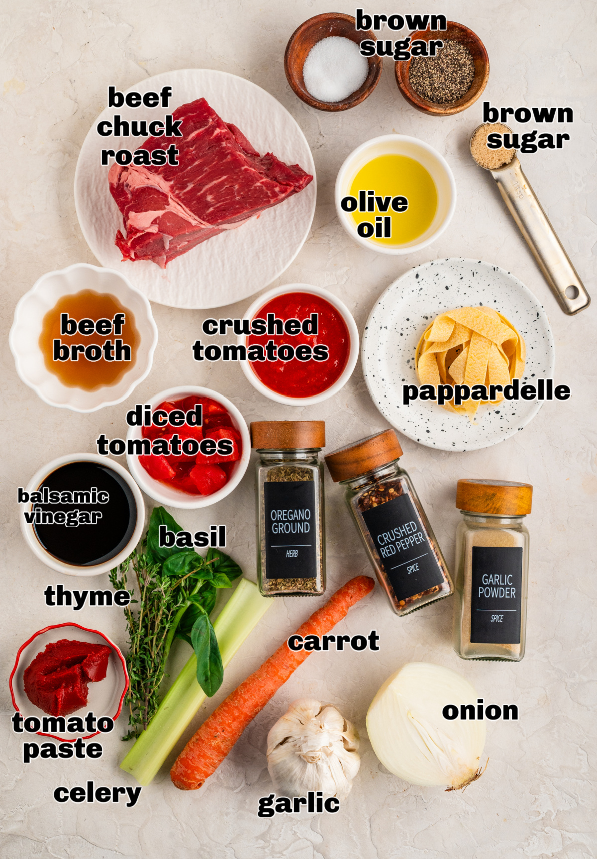 Ingredients for an oven-braised beef rag&ugrave; laid out on a counter, including chuck roast, tomatoes, herbs, aromatics, oil, seasonings, and pappardelle.