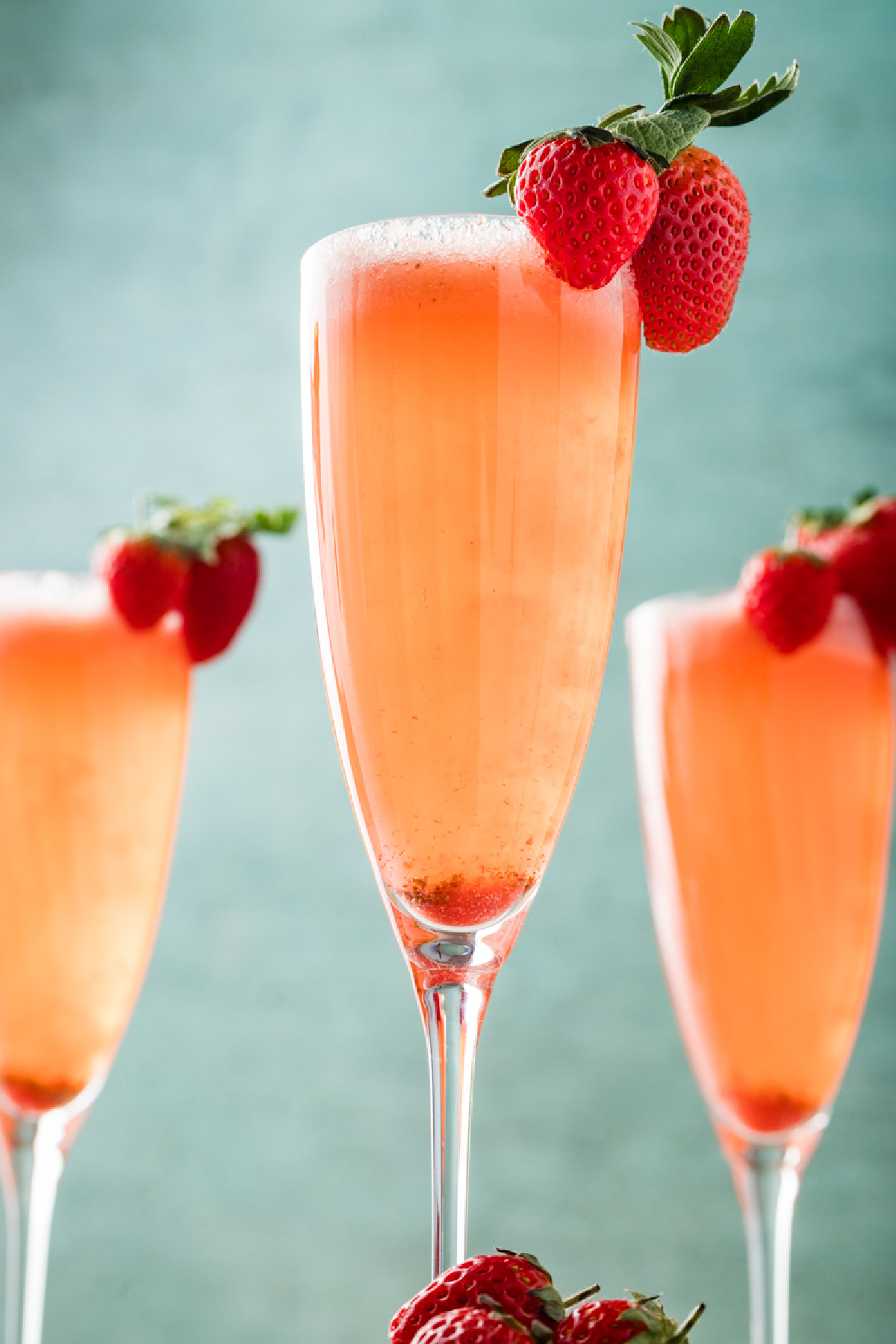 Strawberry bellini in a champagne flute with fresh strawberries clipped to the rim.