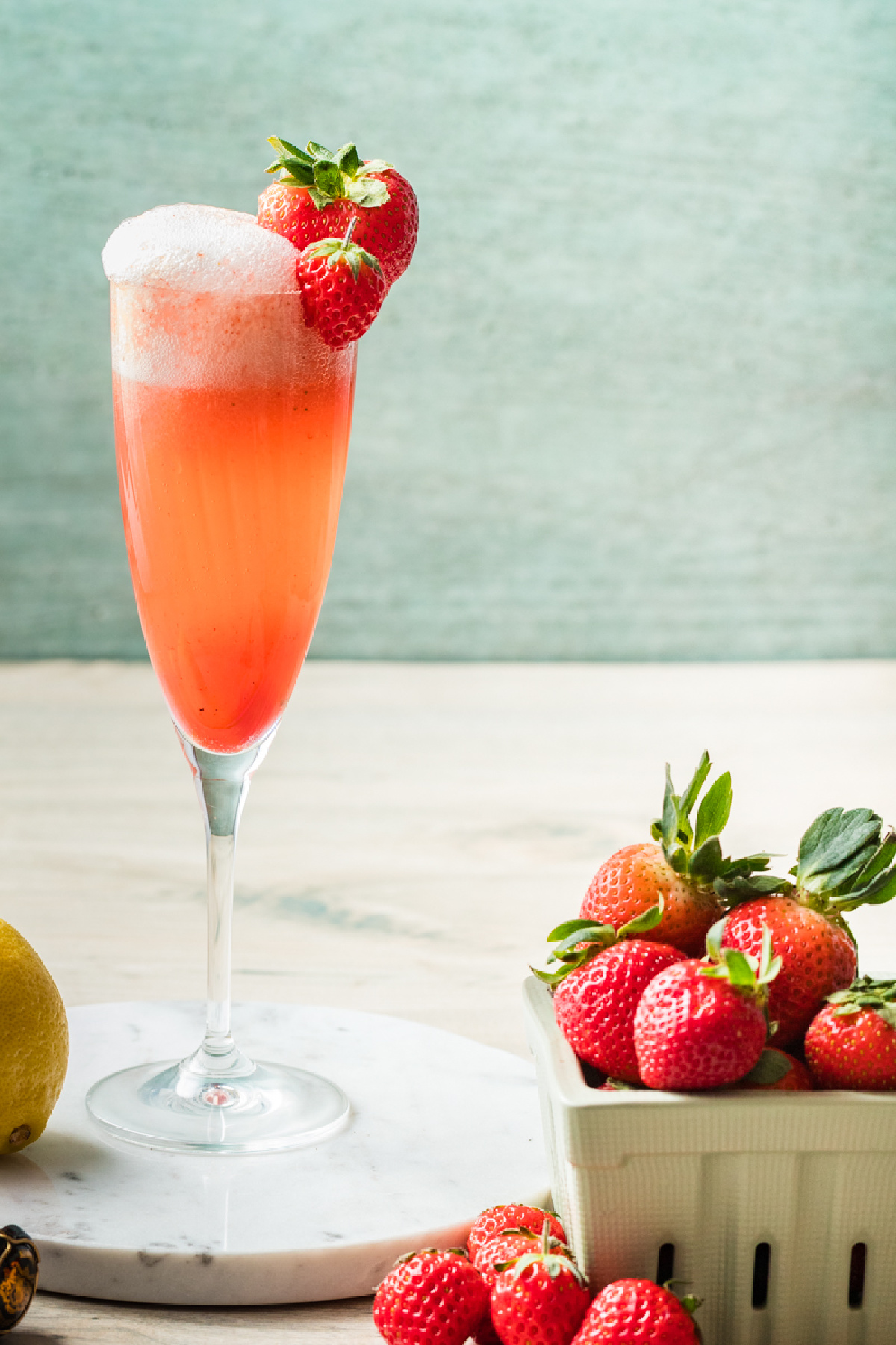 Pale pink strawberry and sparkling wine cocktail served in a champagne flute with fresh strawberries nearby.