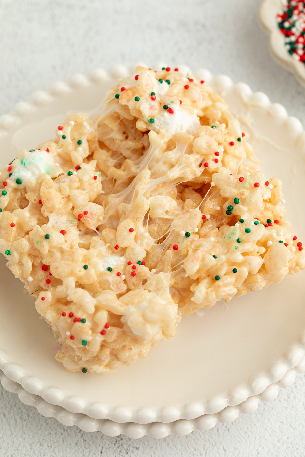 Christmas Sugar Cookie Rice Krispie Treats pulled apart on a plate to show gooey marshmallow stretch and festive holiday sprinkles.