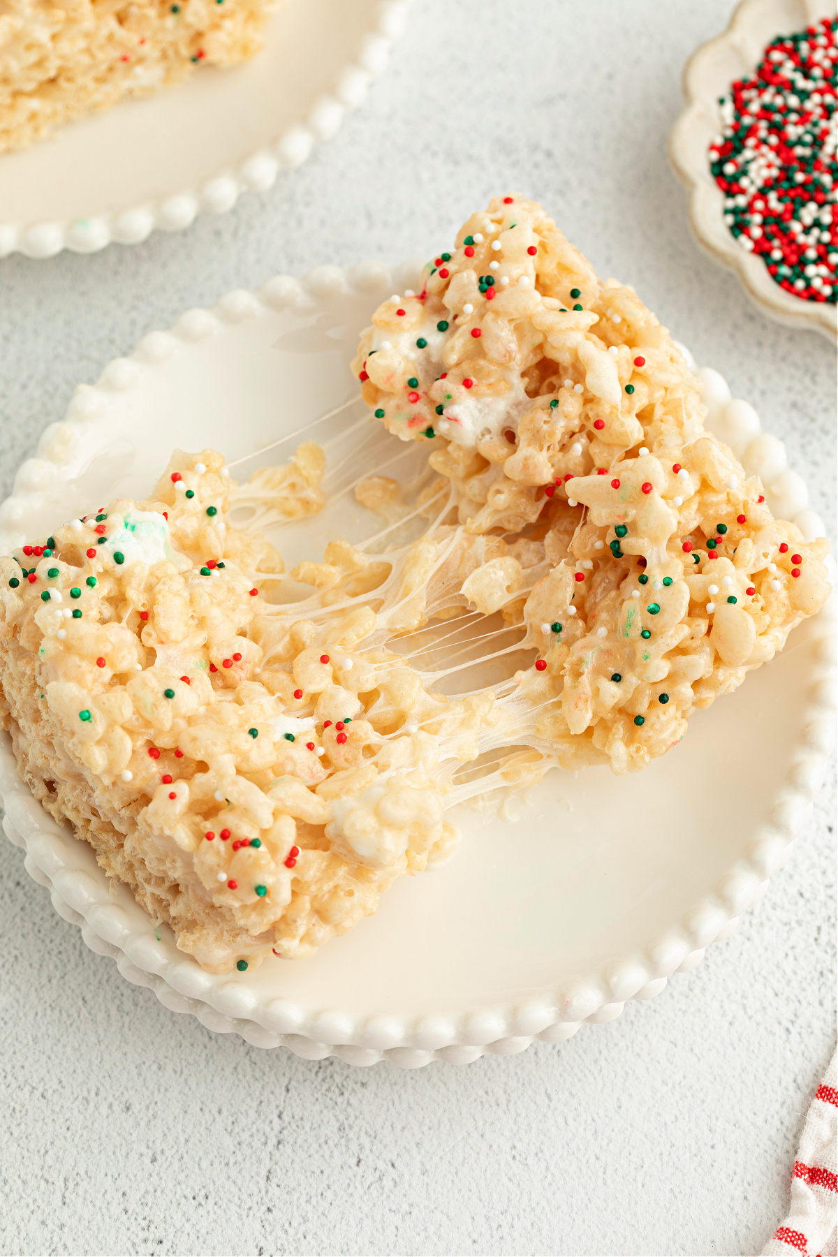 Christmas sugar cookie Rice Krispie treats pulled apart to show gooey marshmallow stretch and holiday sprinkles.