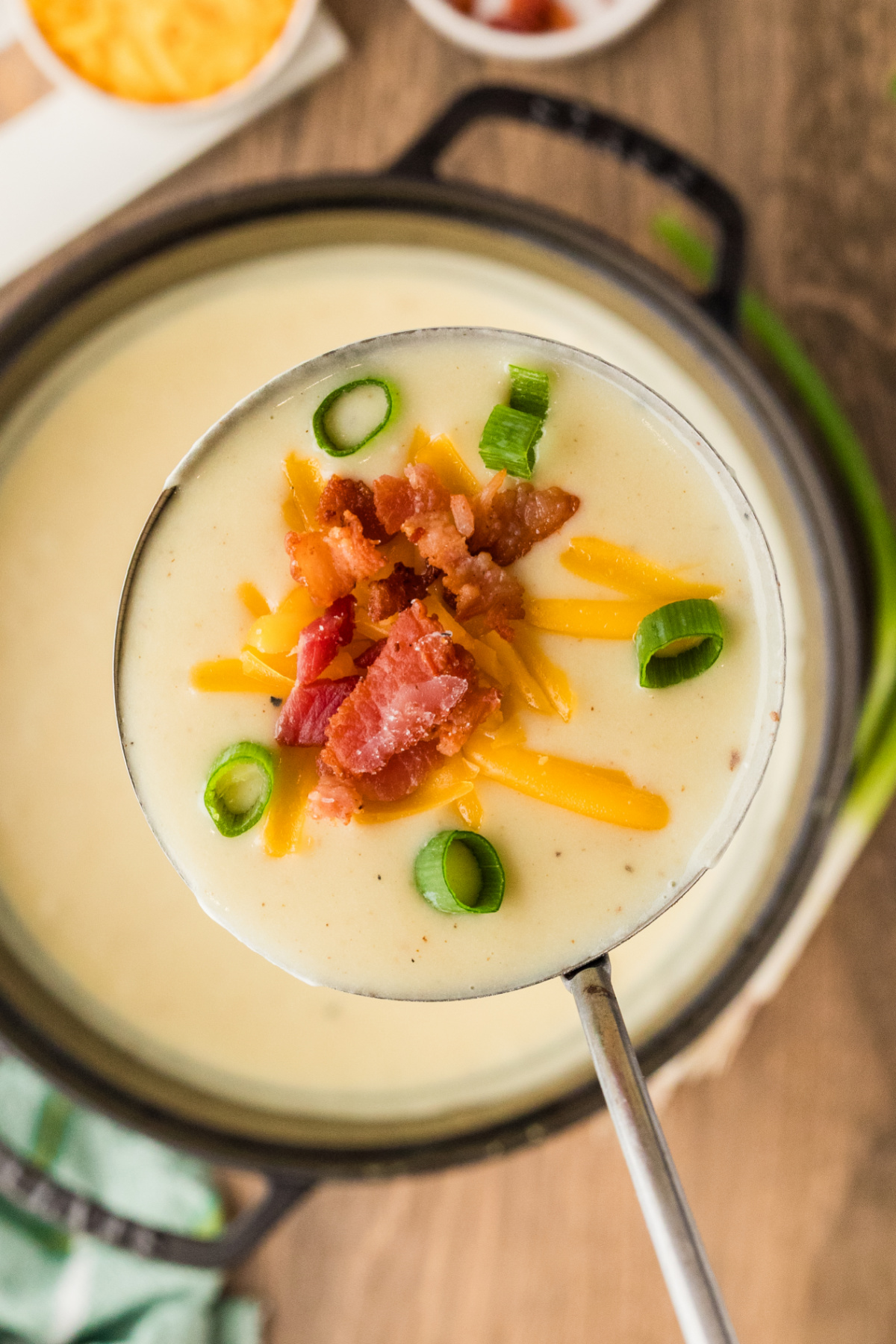 A ladle of loaded baked potato soup showing its thick, creamy texture with bacon, melted cheddar, and scallions.