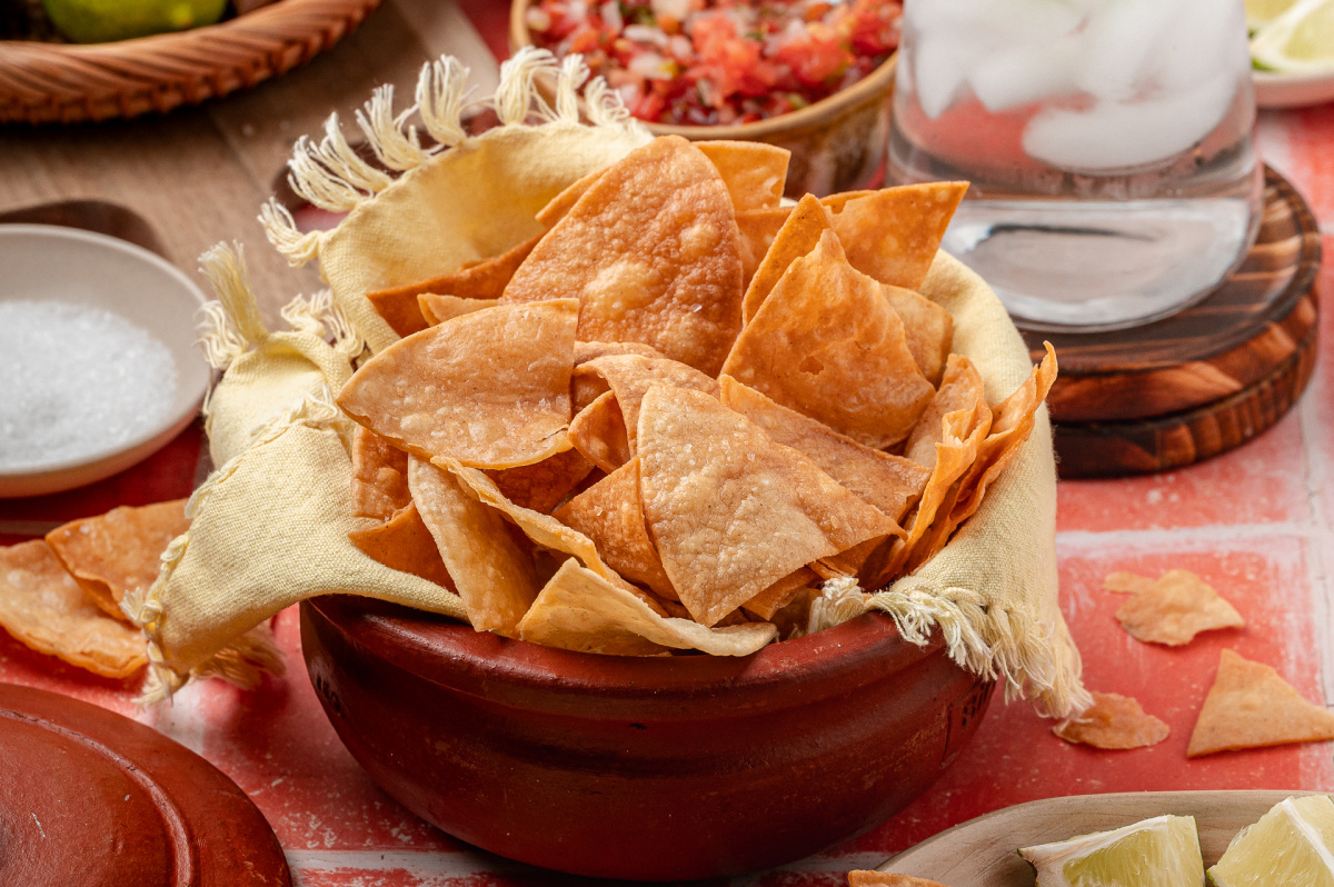 A rustic bowl lined with cloth and filled with easy fried tortilla chips, showing crisp edges and an even golden color ready for serving.