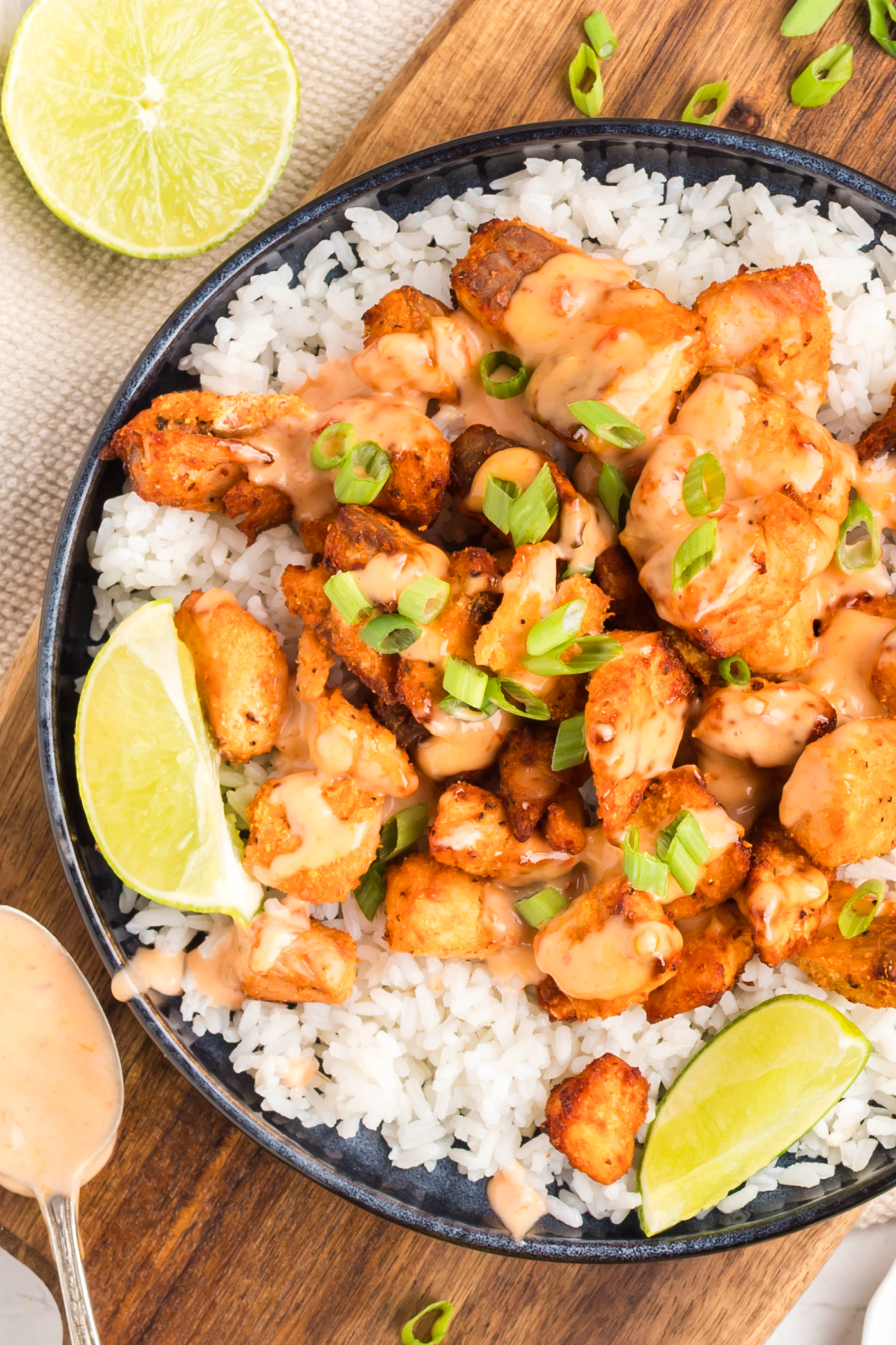 Air fryer bang bang salmon bites served over white rice with creamy sauce drizzled on top, finished with sliced green onions and lime wedges.
