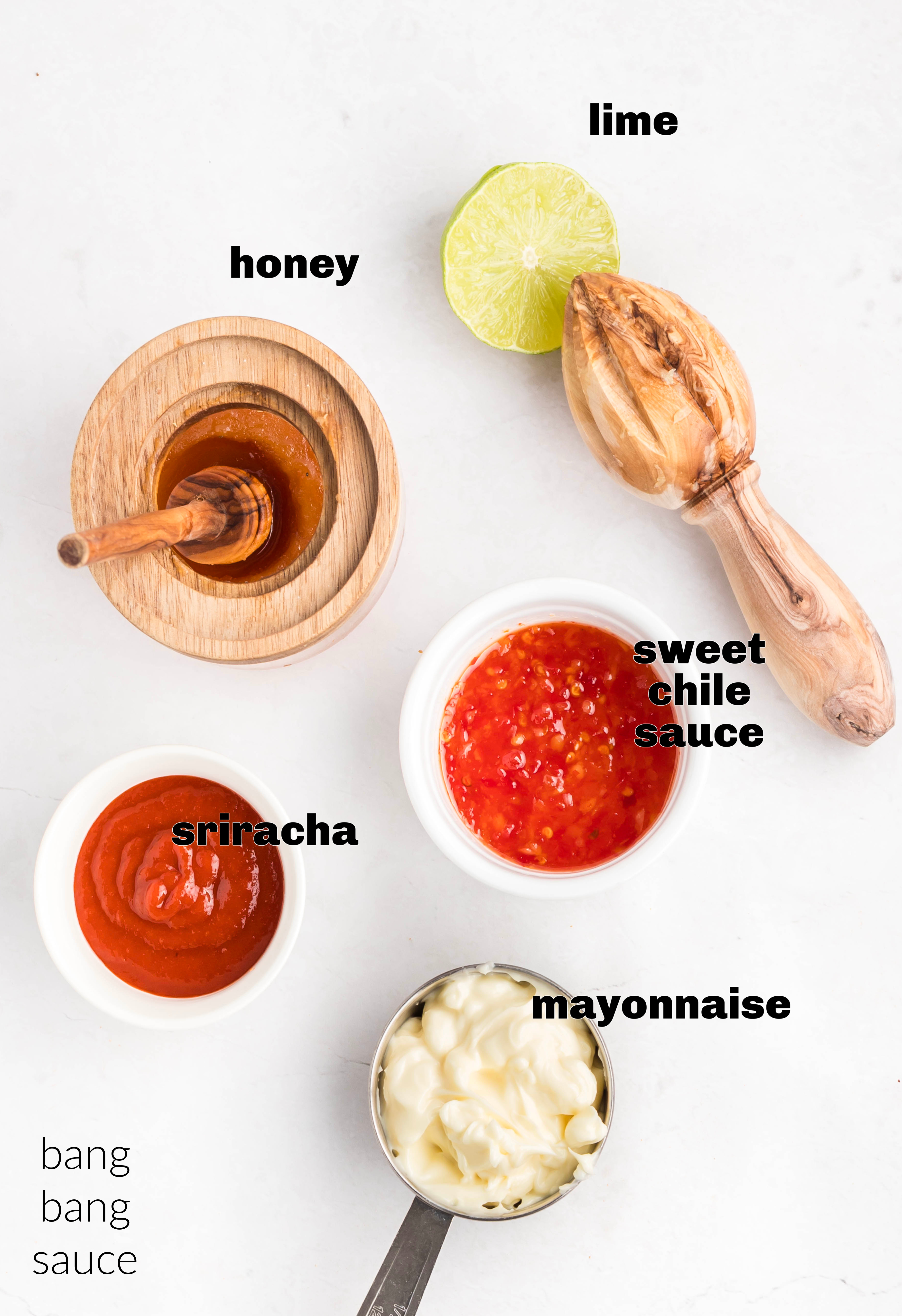 Bang bang sauce ingredients arranged on a white surface, including mayonnaise, sweet chili sauce, sriracha, honey, and fresh lime.