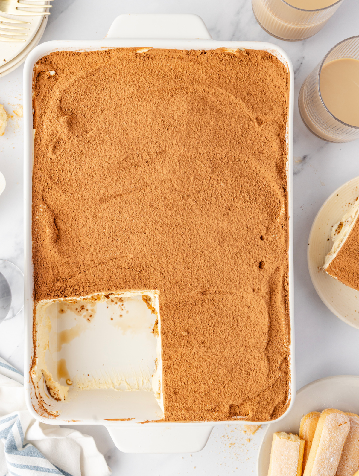 Baileys Irish Cream Tiramisu in a 9&times;13-inch dish with a cocoa-dusted top and a single portion removed to show the creamy mascarpone layer underneath.