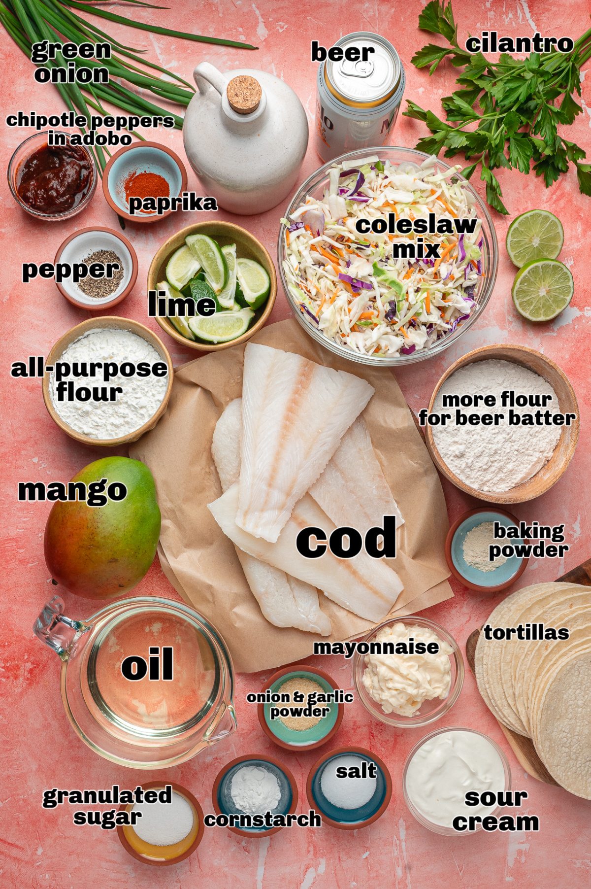 Ingredients for beer-battered fish tacos laid out, including cod, coleslaw mix, mango, beer, tortillas, and chipotle lime sauce components.