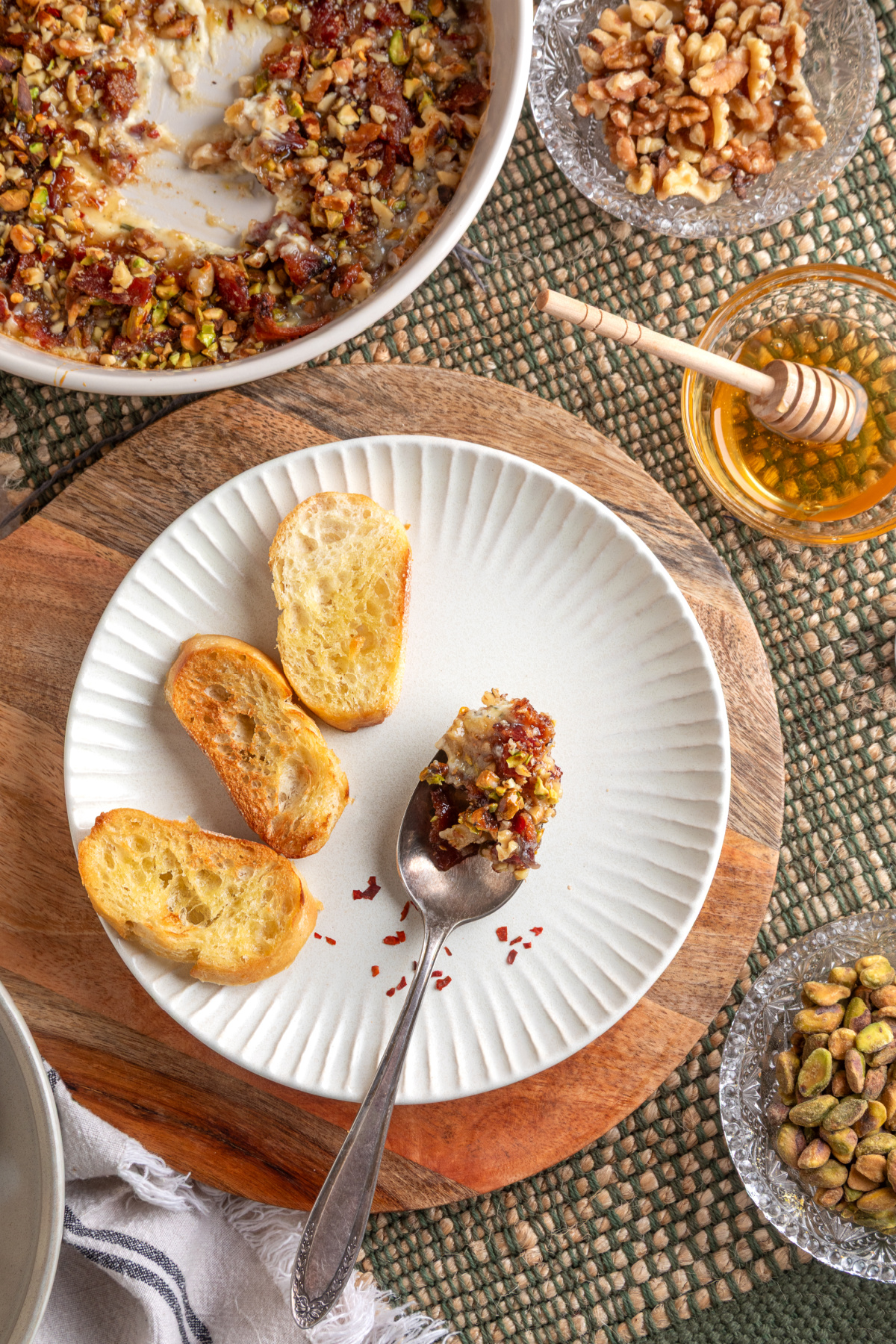 A spoonful of Boursin Bacon Pistachio & Fig Dip served on a plate with toasted bread, honey, pistachios, and walnuts.