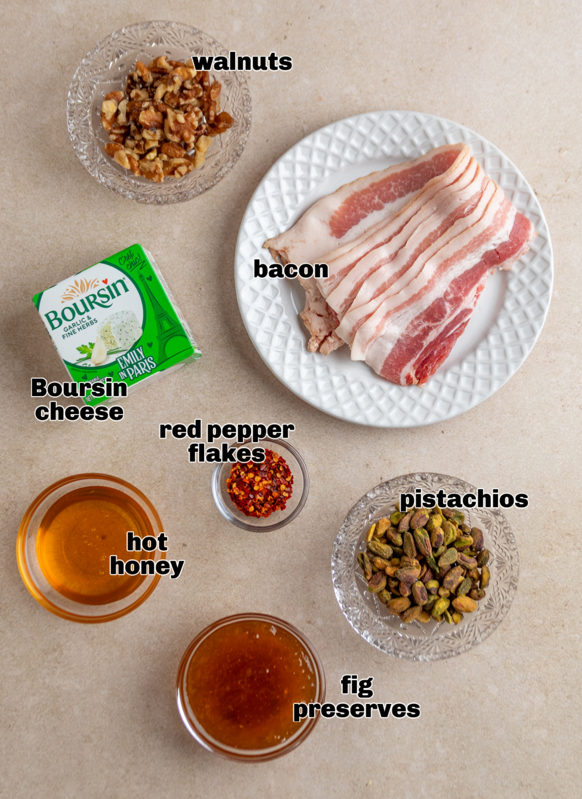 Ingredients for a baked Boursin dip including Boursin garlic herb cheese, thick-cut bacon, fig preserves, pistachios, walnuts, red pepper flakes, and hot honey.