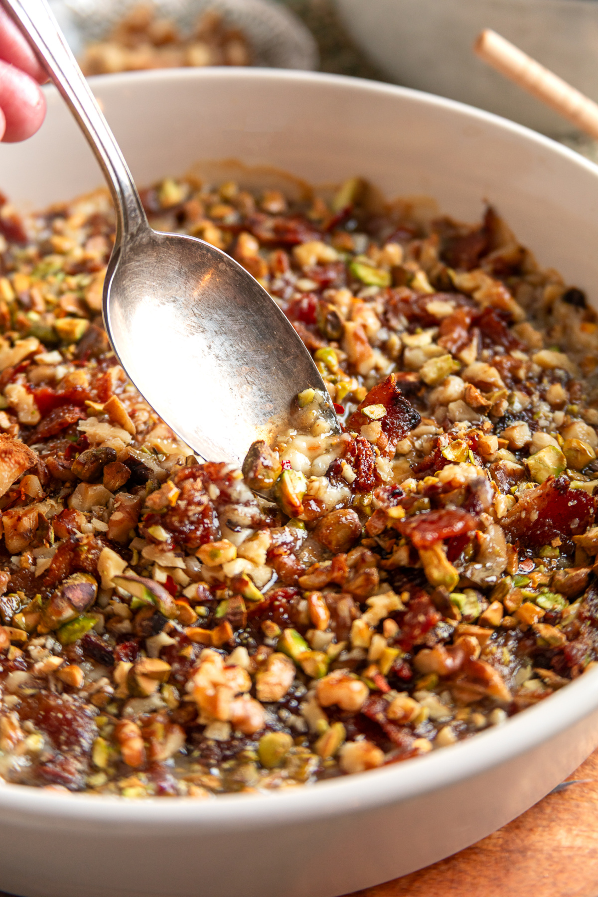 A spoon scooping into a baked Boursin dip with bacon, fig preserves, pistachios, and walnuts while the cheese is still soft and melted.