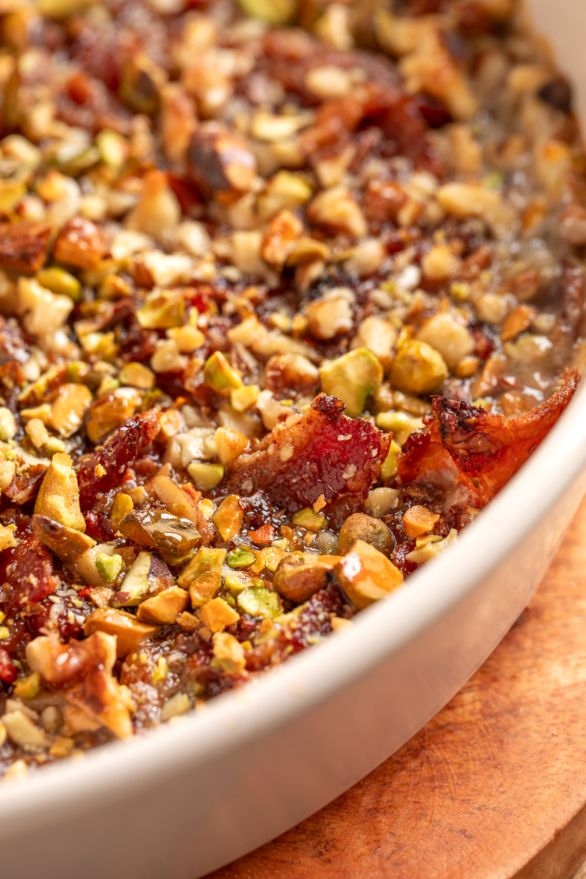 Close-up of Boursin Bacon Pistachio & Fig Dip showing crisp bacon, chopped pistachios, walnuts, and bubbling cheese at the edges.