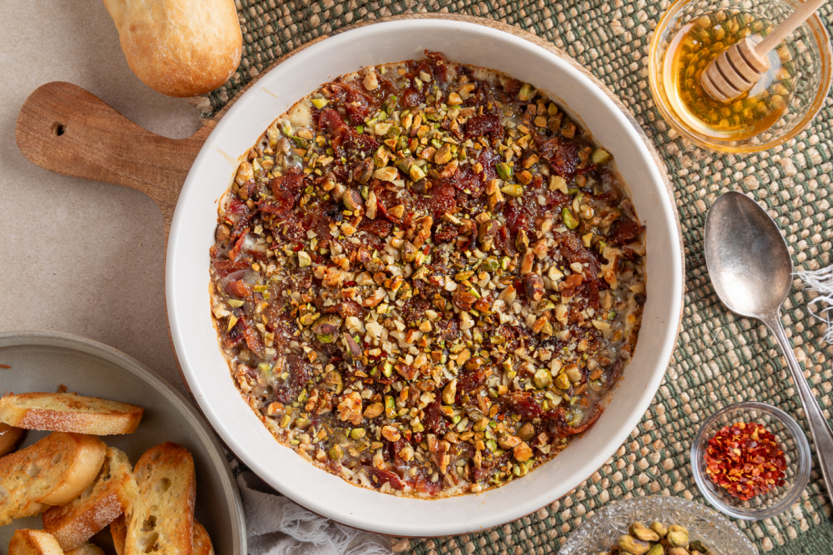 Overhead view of Boursin Bacon Pistachio & Fig Dip baked until bubbly and topped with bacon, pistachios, walnuts, and hot honey.