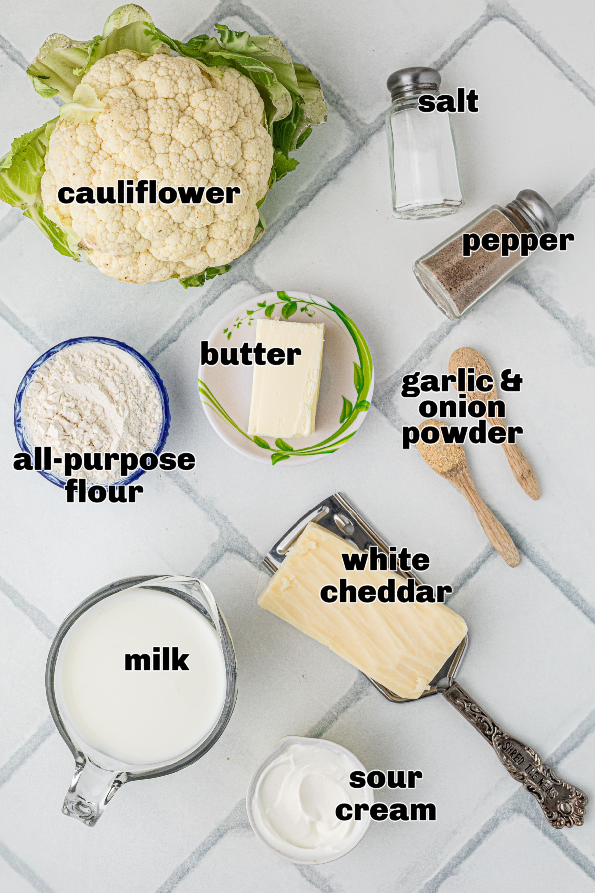 Ingredients for baked cauliflower mac and cheese, including cauliflower, white cheddar, milk, butter, flour, sour cream, salt, pepper, and garlic and onion powder.