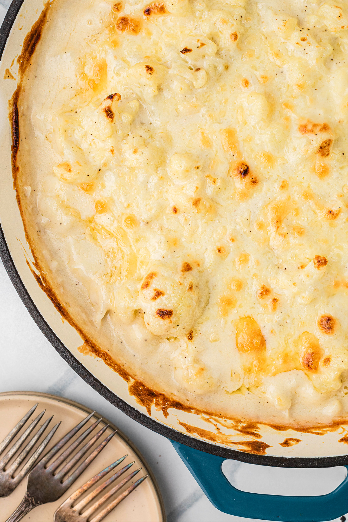 Cauliflower mac and cheese baked in a skillet with bubbling edges and a melted cheddar cheese topping.
