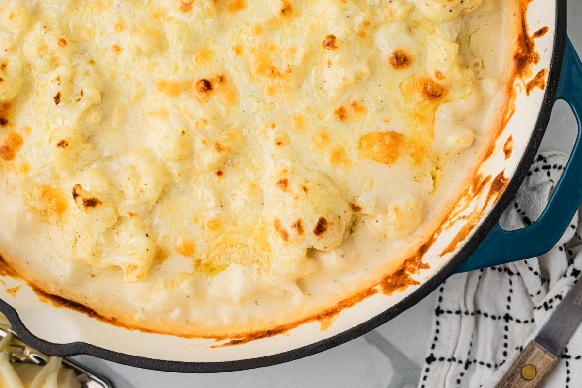 Close-up of baked cauliflower in a creamy cheese sauce with lightly browned spots and bubbling edges in a skillet.