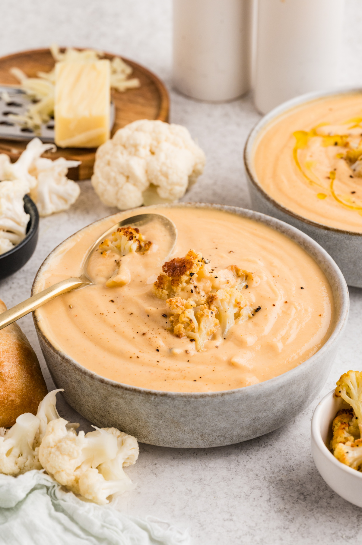 Creamy cauliflower soup topped with roasted cauliflower florets, black pepper, and olive oil, served with bread on the side.