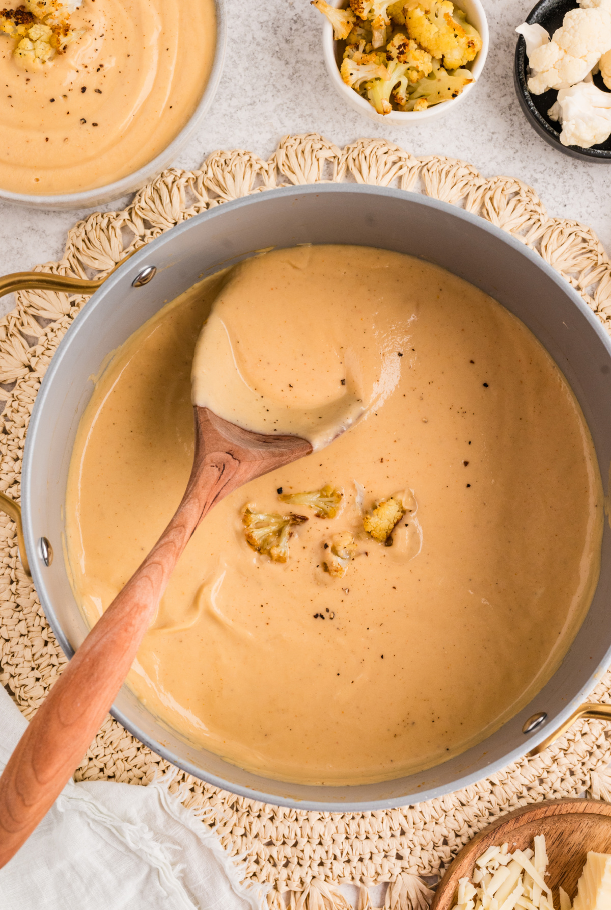 Roasted Cauliflower Soup being stirred in a pot with a wooden spoon and finished with roasted cauliflower florets.