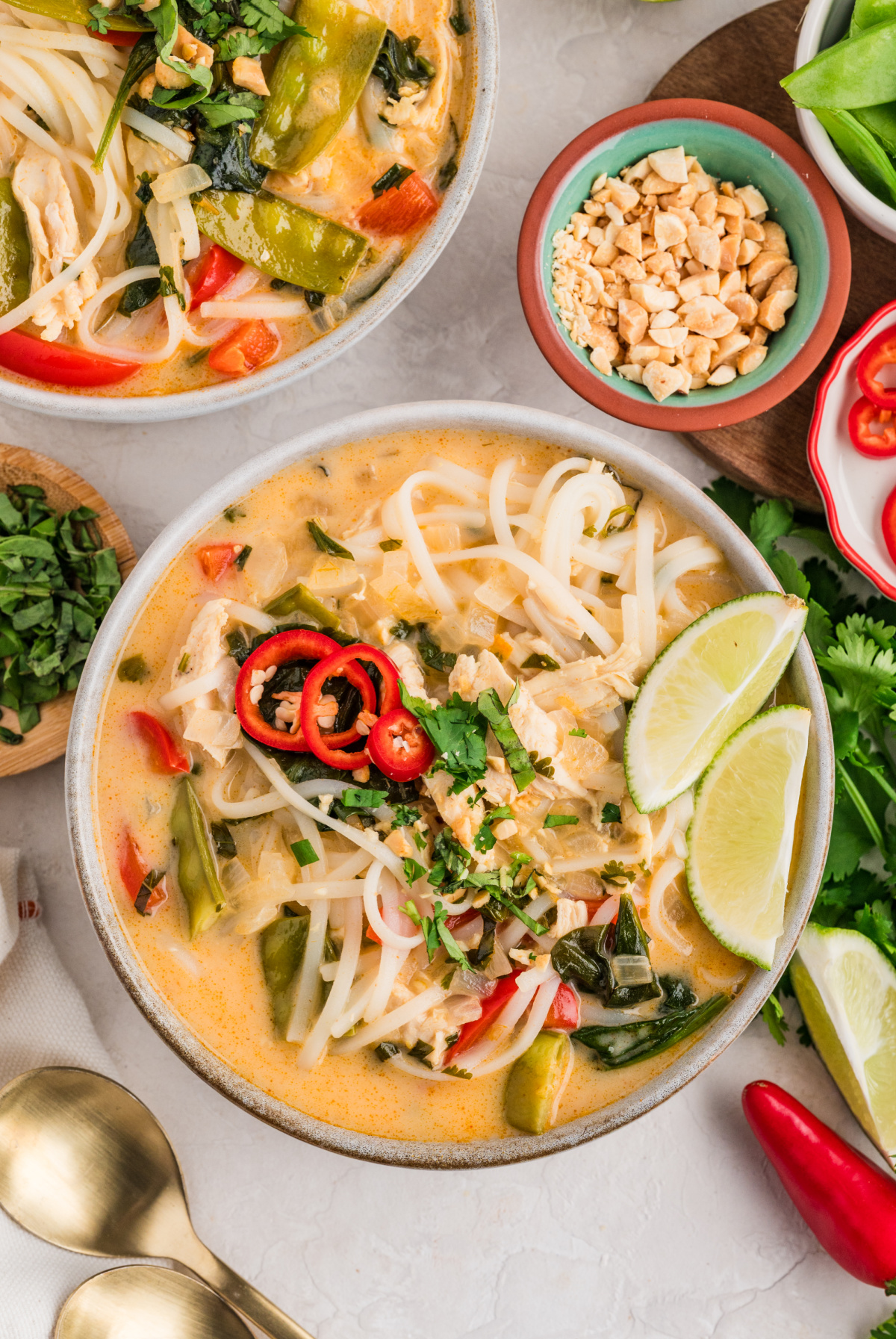 Thai chicken curry soup with coconut milk, rice noodles, shredded chicken, red bell pepper, snow peas, and fresh herbs, finished with lime and sliced red chili.