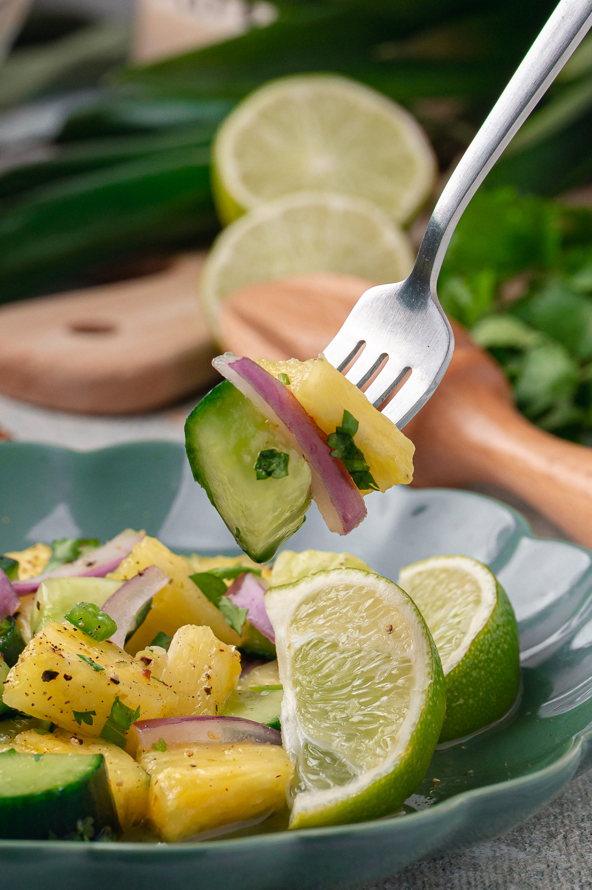 Chilled pineapple and cucumber salad resting in a ceramic bowl with lime slices and cilantro.