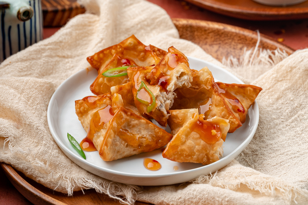 Crab rangoon arranged on a plate, fried until crisp and drizzled with sweet and spicy dipping sauce.