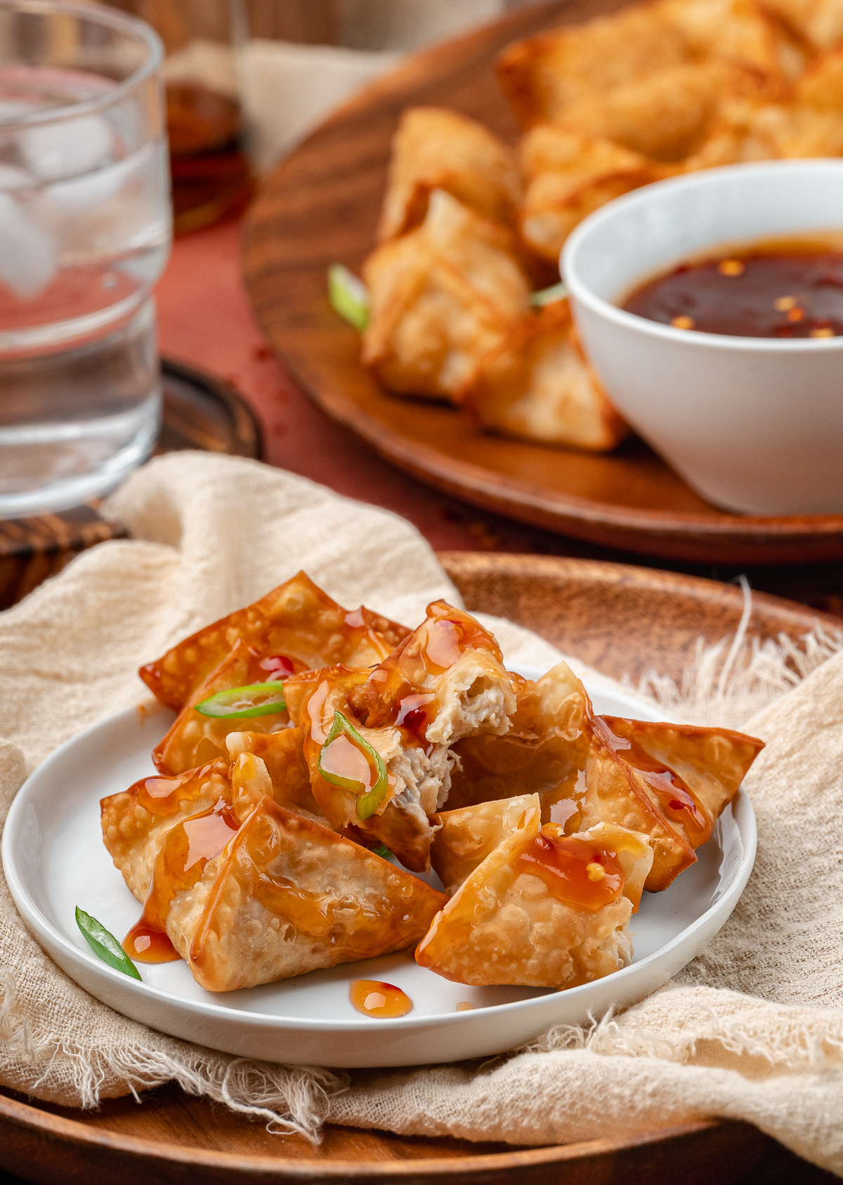 Crisp fried wontons filled with creamy crab and drizzled with sweet and spicy dipping sauce on a small plate.