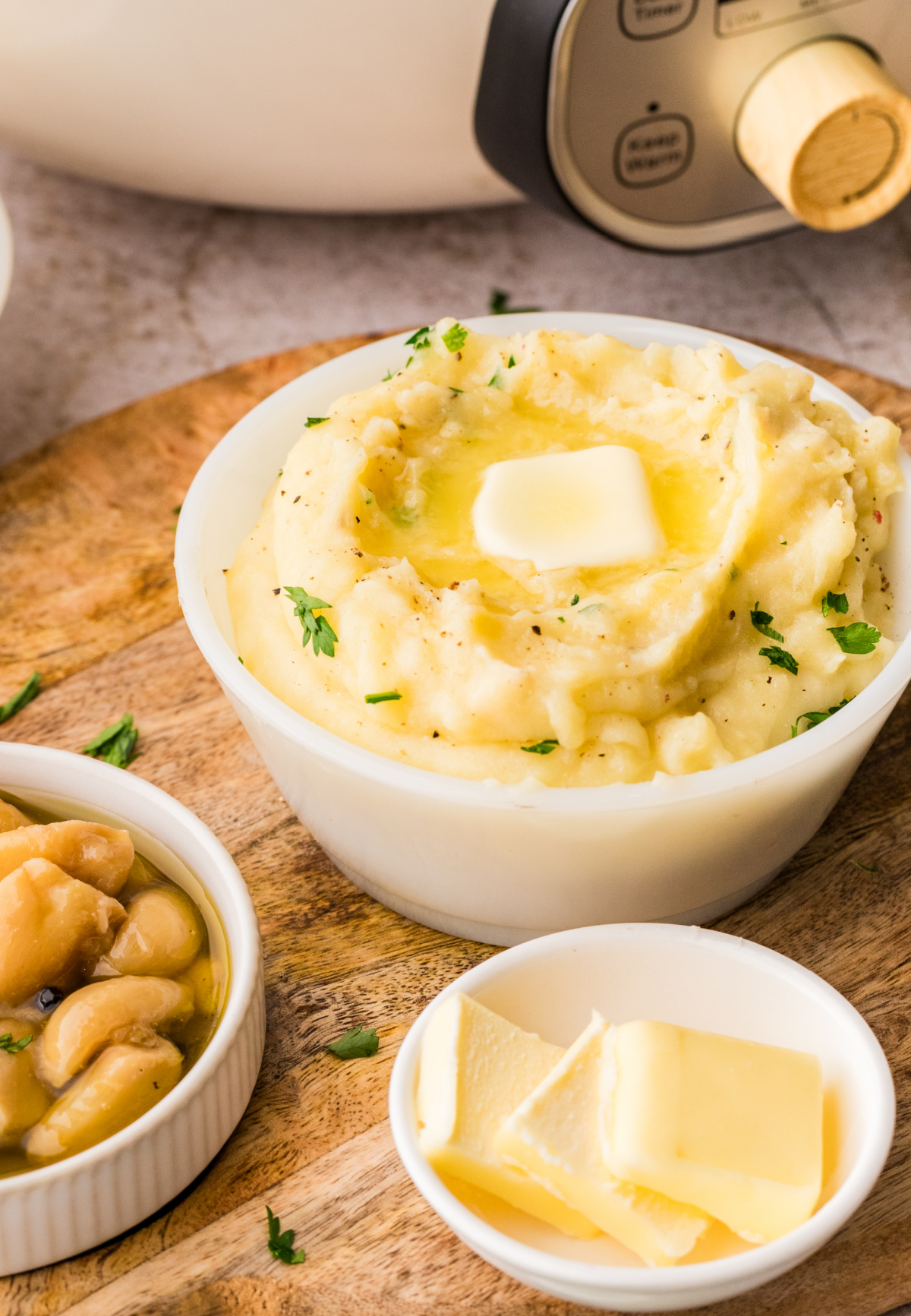 Slow cooker garlic confit mashed potatoes served in a bowl with butter melting on top and confit garlic nearby, ready to serve.
