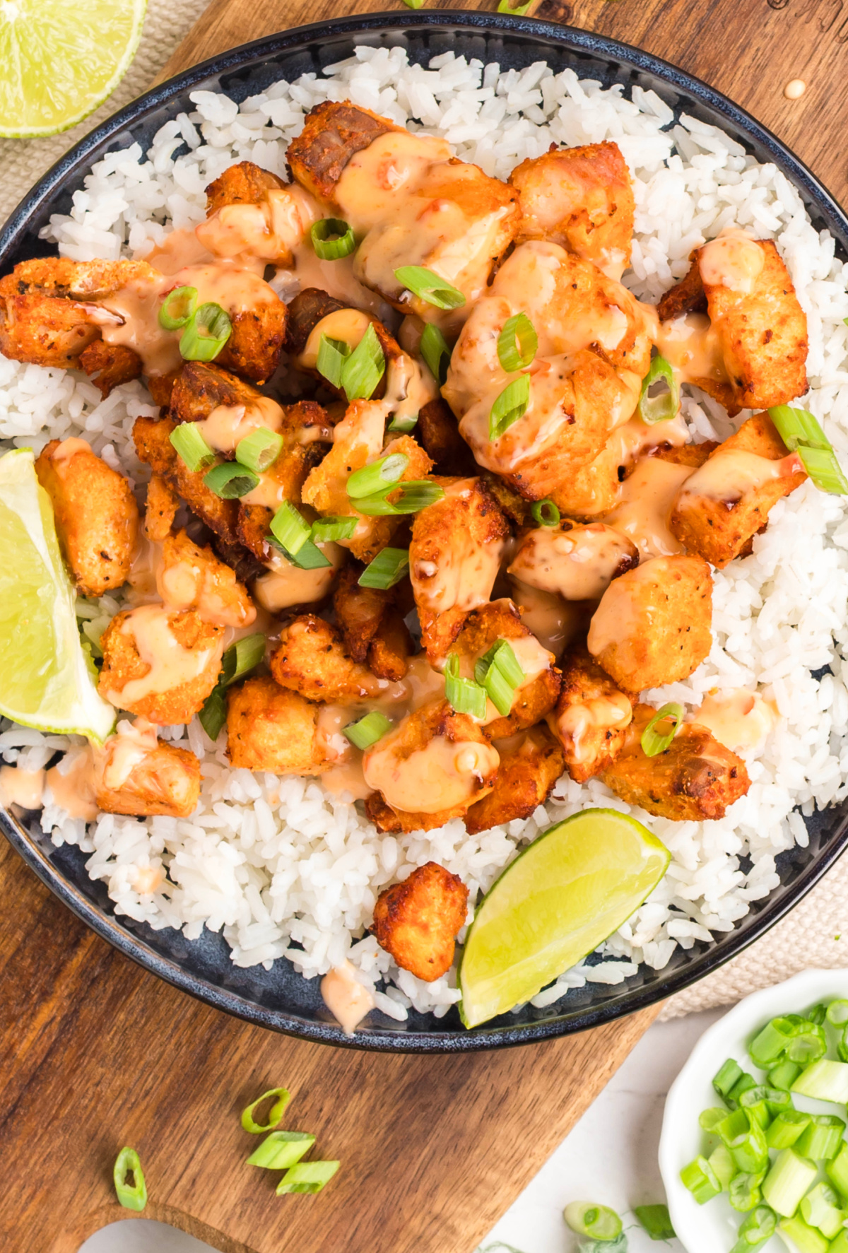 Air fryer bang bang salmon bites served over white rice with creamy sauce and sliced green onions.