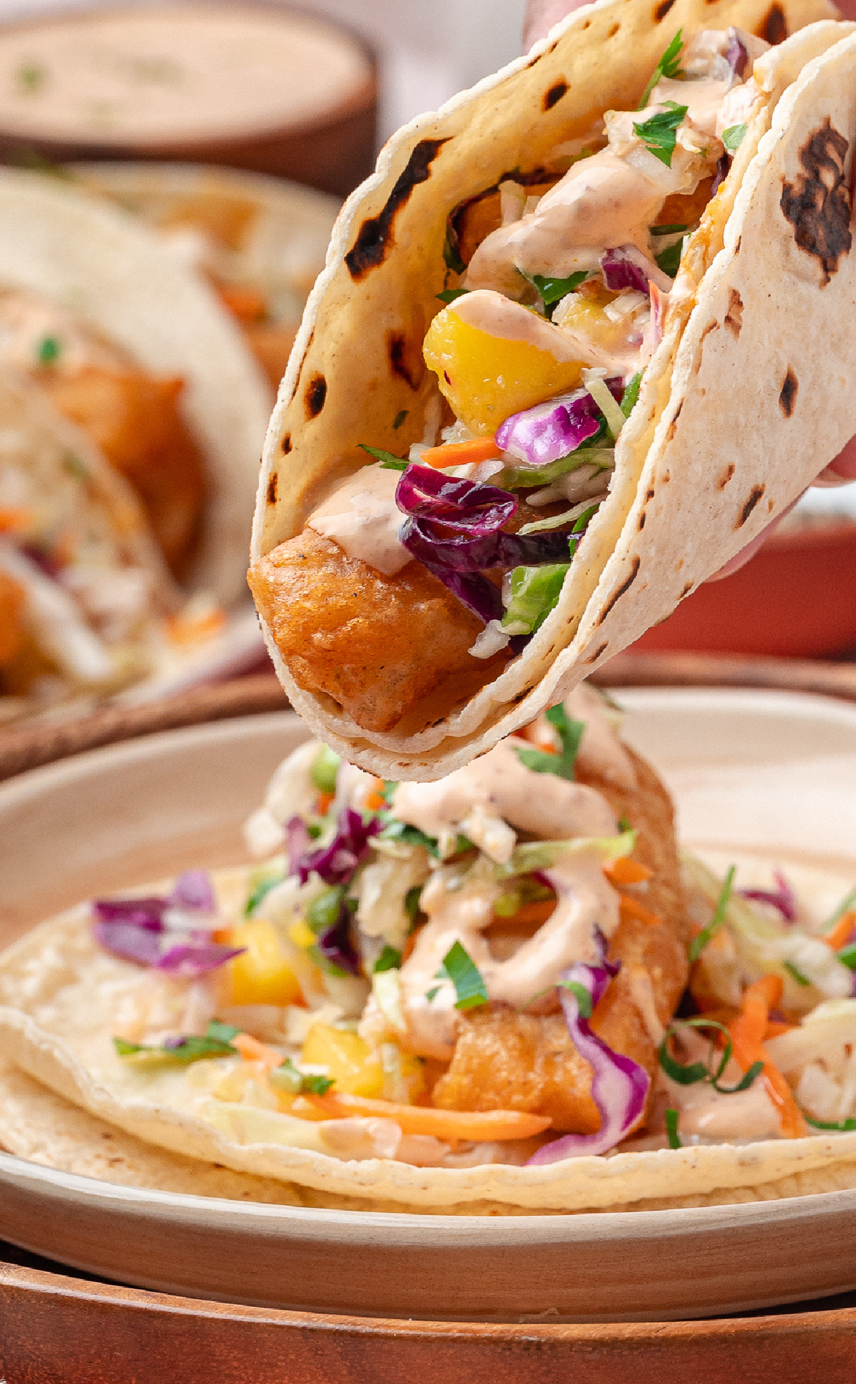Close-up of crispy beer-battered cod in a corn tortilla with mango slaw and chipotle lime sauce.