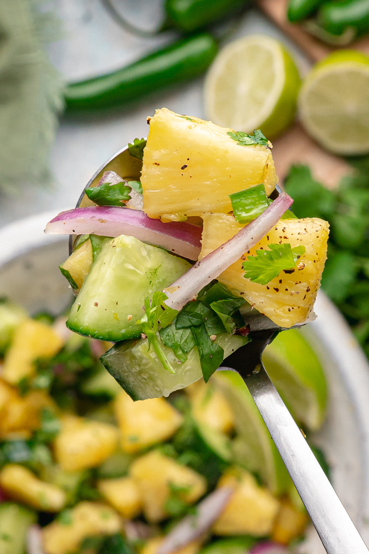Fork lifting a bite of pineapple and cucumber salad with red onion, cilantro, and lime.