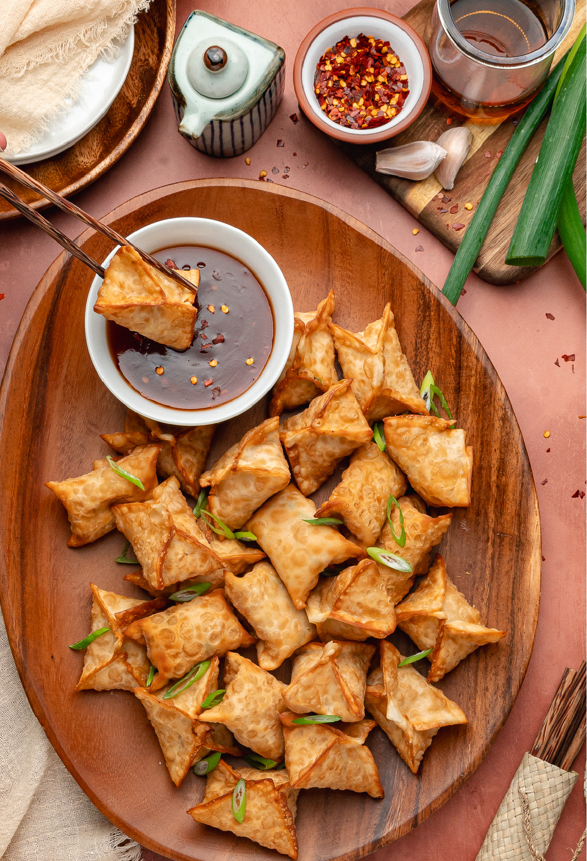 Fried crab rangoon piled on a serving platter with crisp golden wrappers and a bowl of sweet and spicy dipping sauce.