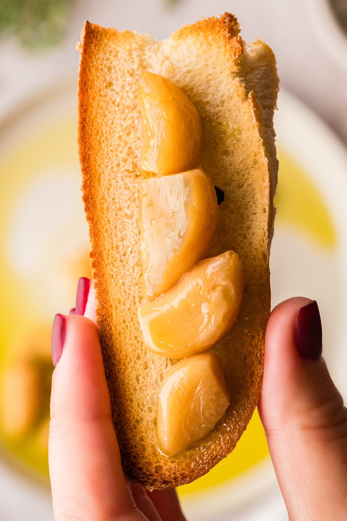 Soft garlic cloves resting on toasted bread, held upright and ready to spread.