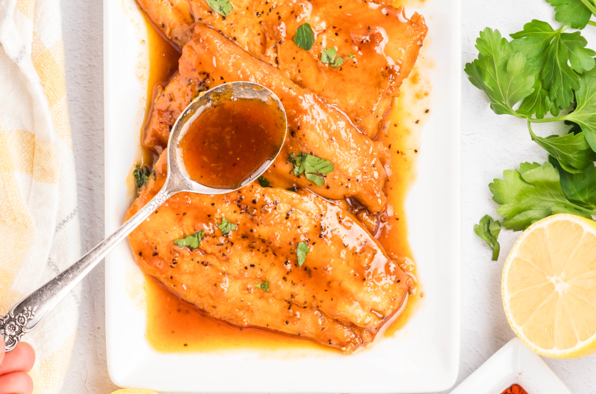 Glazed salmon fillets on a platter being spooned with warm honey soy glaze during the final basting step.