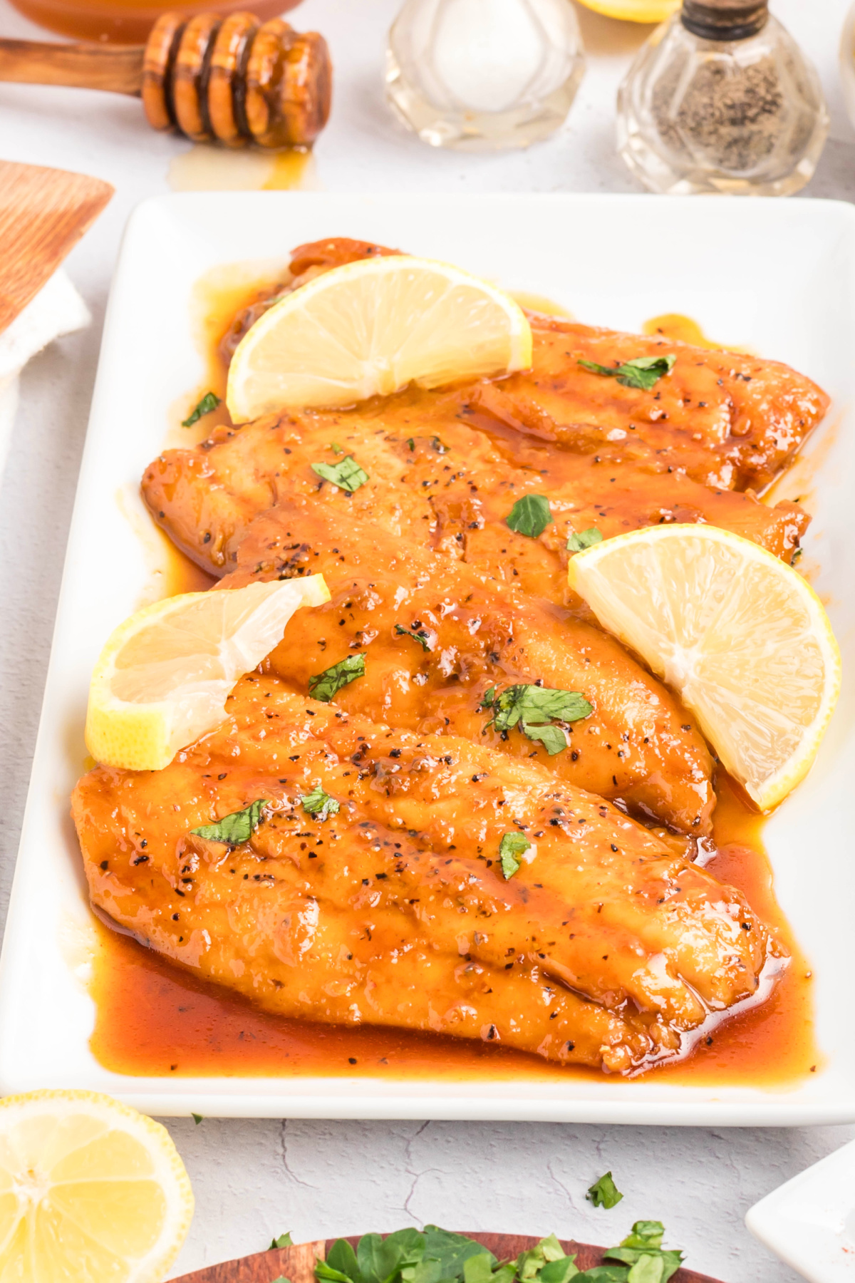 Pan seared salmon fillets finished with a honey soy glaze, cracked black pepper, and chopped parsley on a white serving platter.