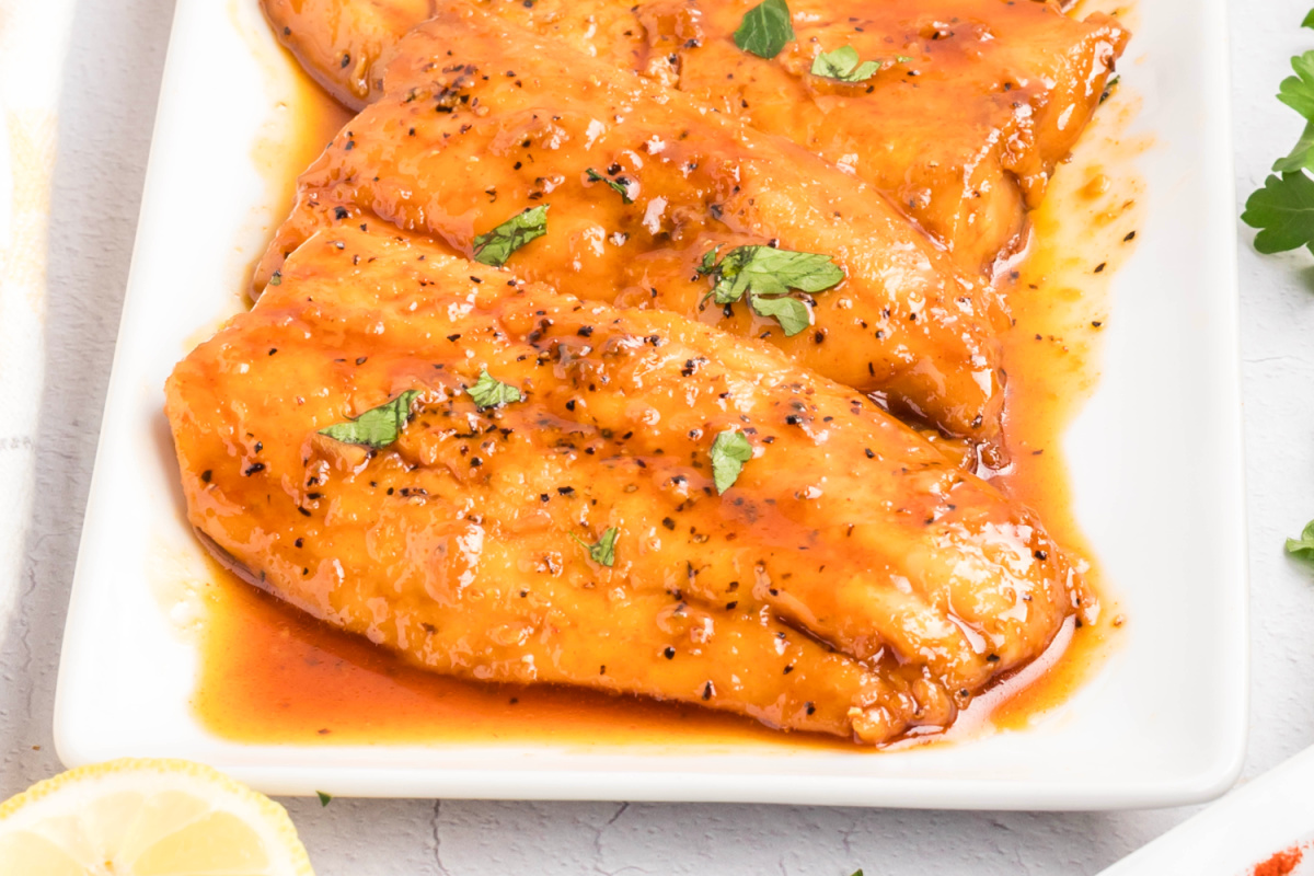 Honey glazed salmon arranged on a white platter with a smooth honey glaze, cracked black pepper, and chopped parsley.