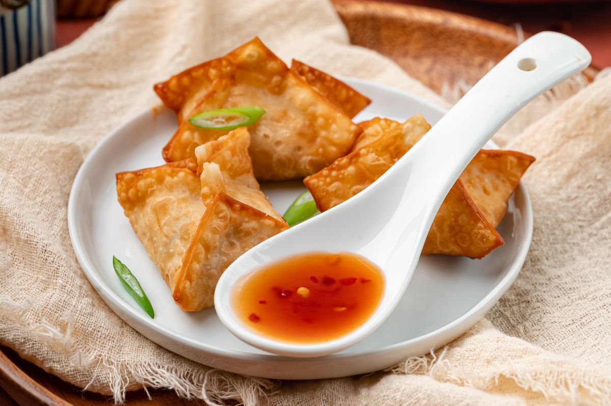 Homemade crab rangoon with crisp wonton wrappers served alongside a sweet and spicy dipping sauce.