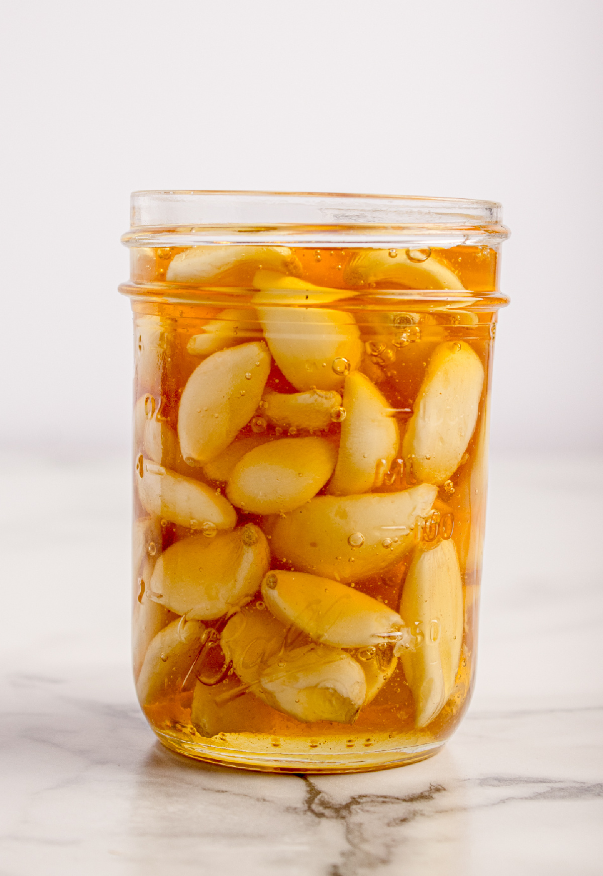 Fermented honey garlic after several weeks, with softened whole garlic cloves fully submerged in loosened honey.