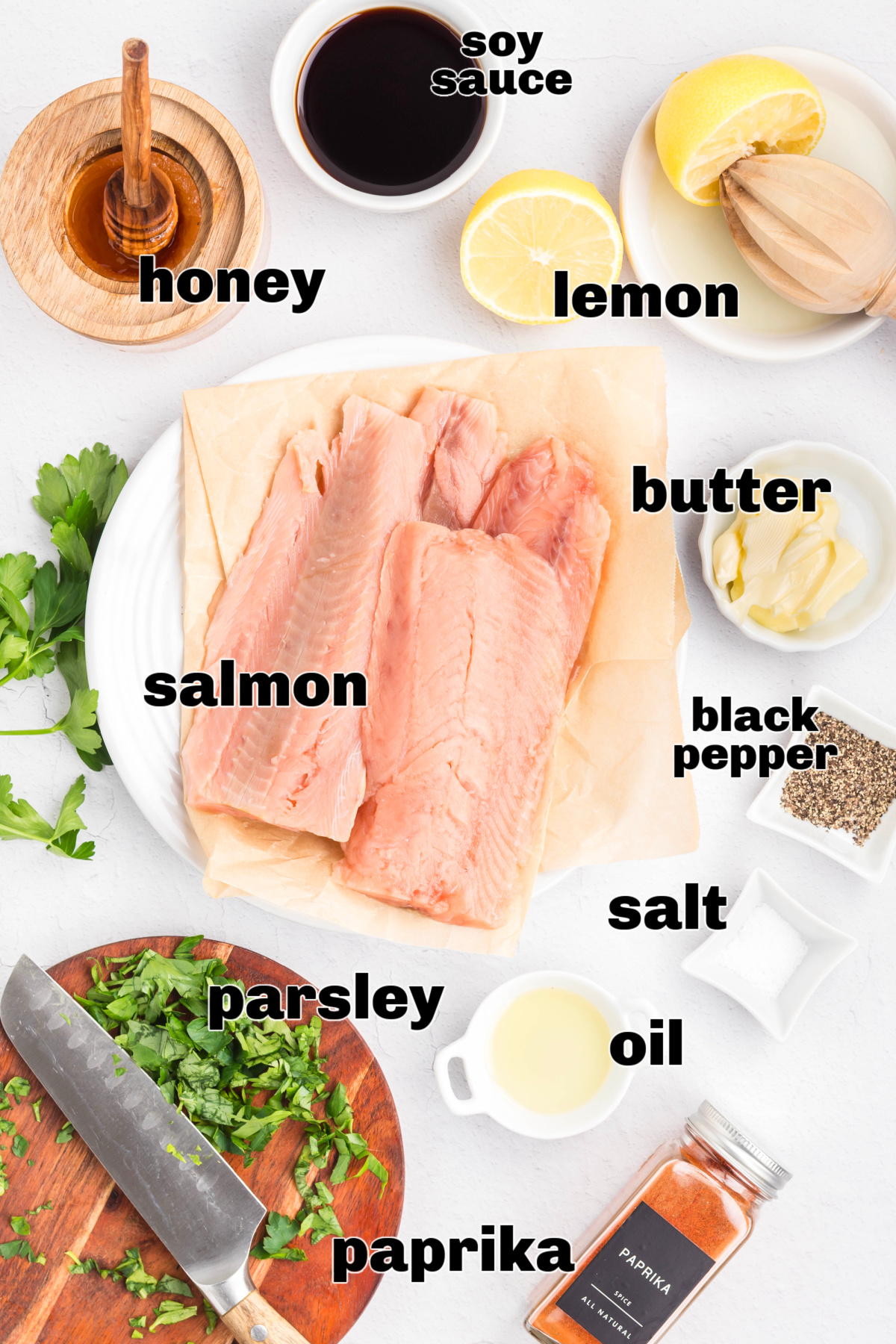 Ingredients for glazed salmon laid out on a counter, including raw salmon fillets, honey, soy sauce, lemon, butter, oil, salt, black pepper, paprika, and parsley.