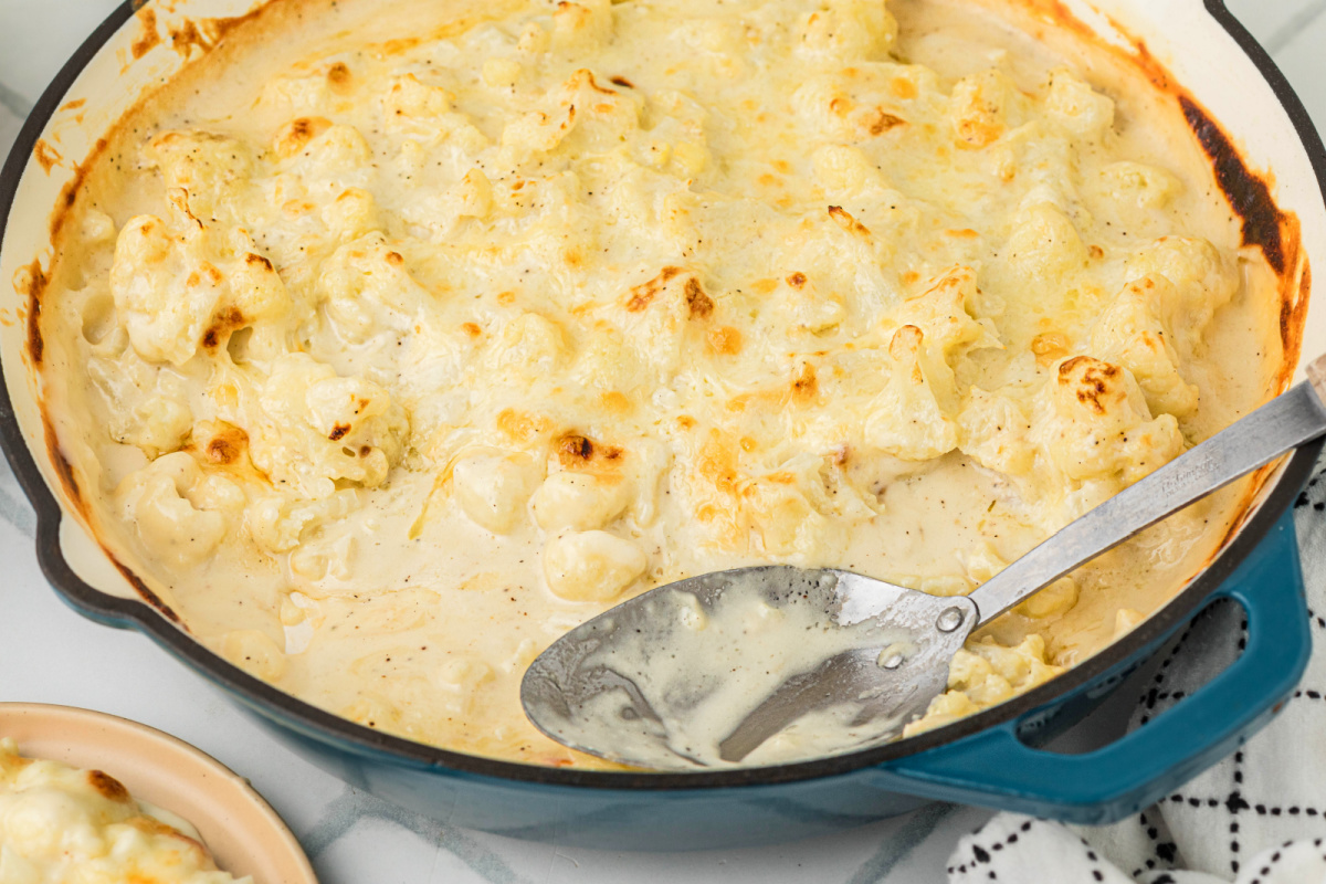 Cauliflower mac and cheese scooped from a skillet, showing tender cauliflower coated in a creamy cheddar cheese sauce.