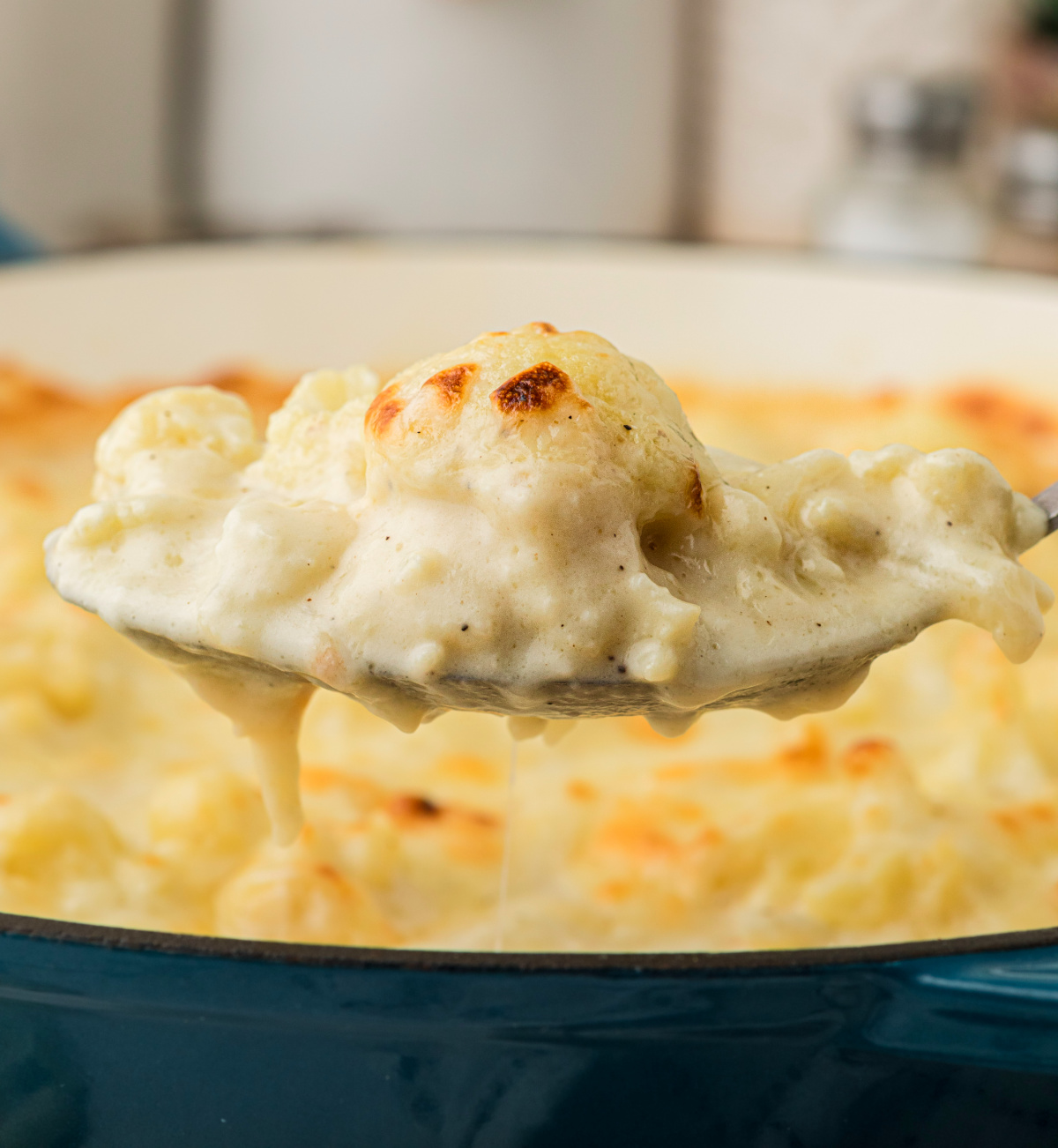 Spoonful of baked cauliflower coated in a thick, creamy cheese sauce, lifting from a skillet while still hot and melty.