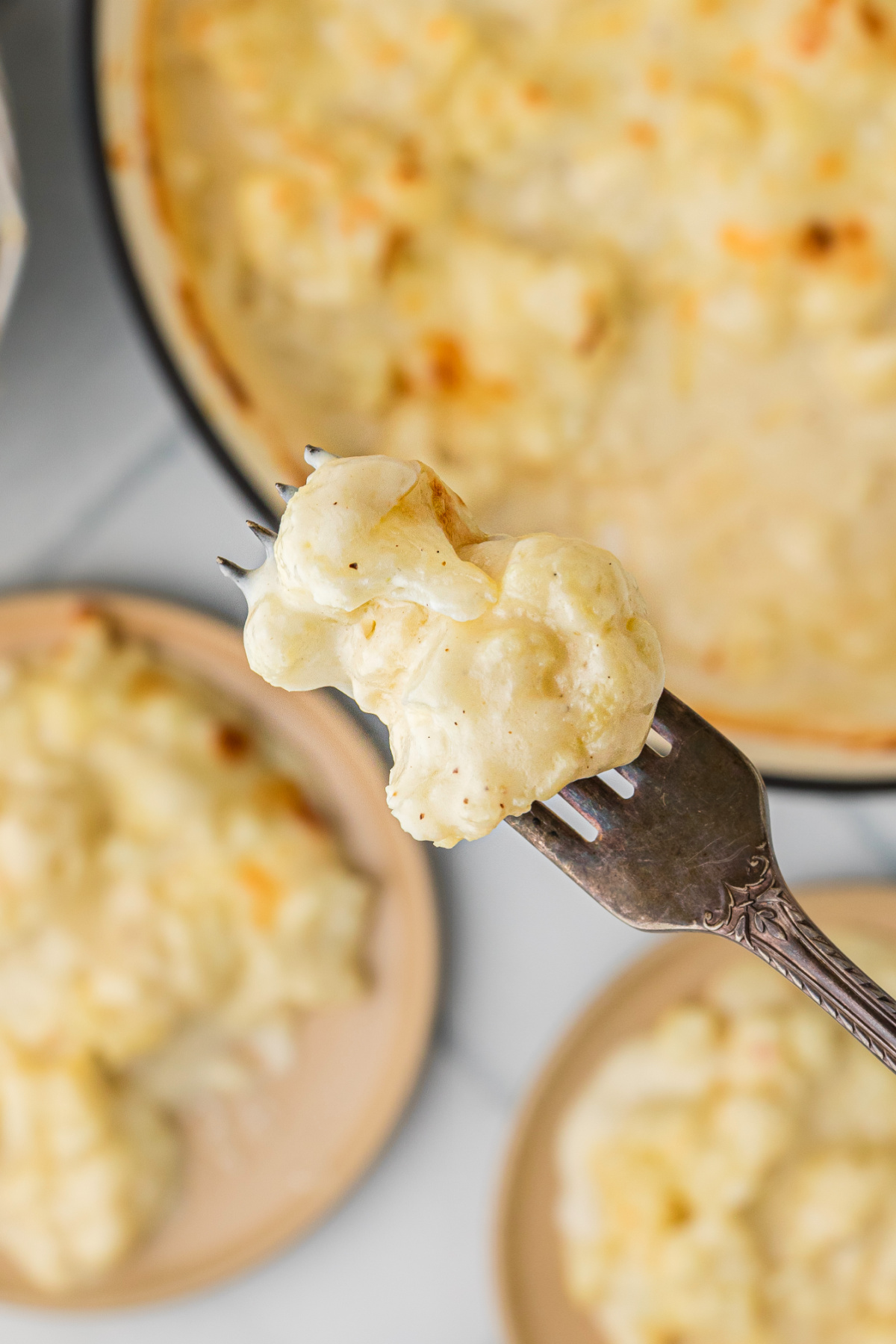 Forkful of baked cauliflower coated in a smooth, creamy cheese sauce, showing the soft texture and rich coating.