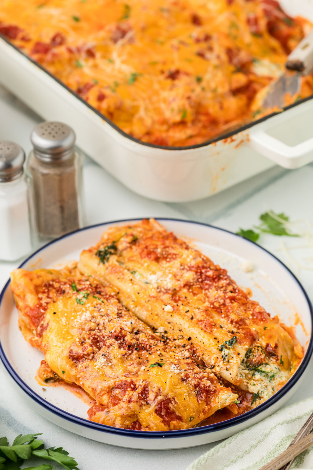 Plated manicotti filled with ricotta and spinach, topped with marinara sauce, melted cheddar, and Parmesan