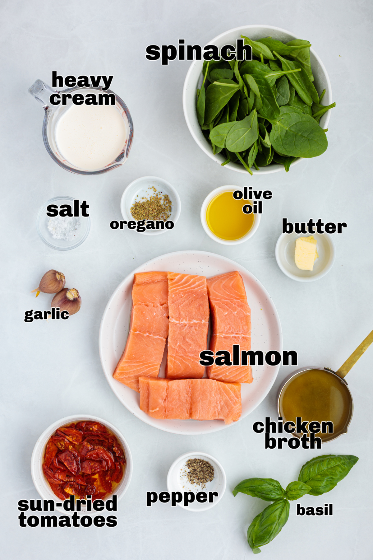 Ingredients for Tuscan salmon including salmon fillets, heavy cream, spinach, sun-dried tomatoes, garlic, olive oil, butter, chicken broth, oregano, salt, pepper, and fresh basil.